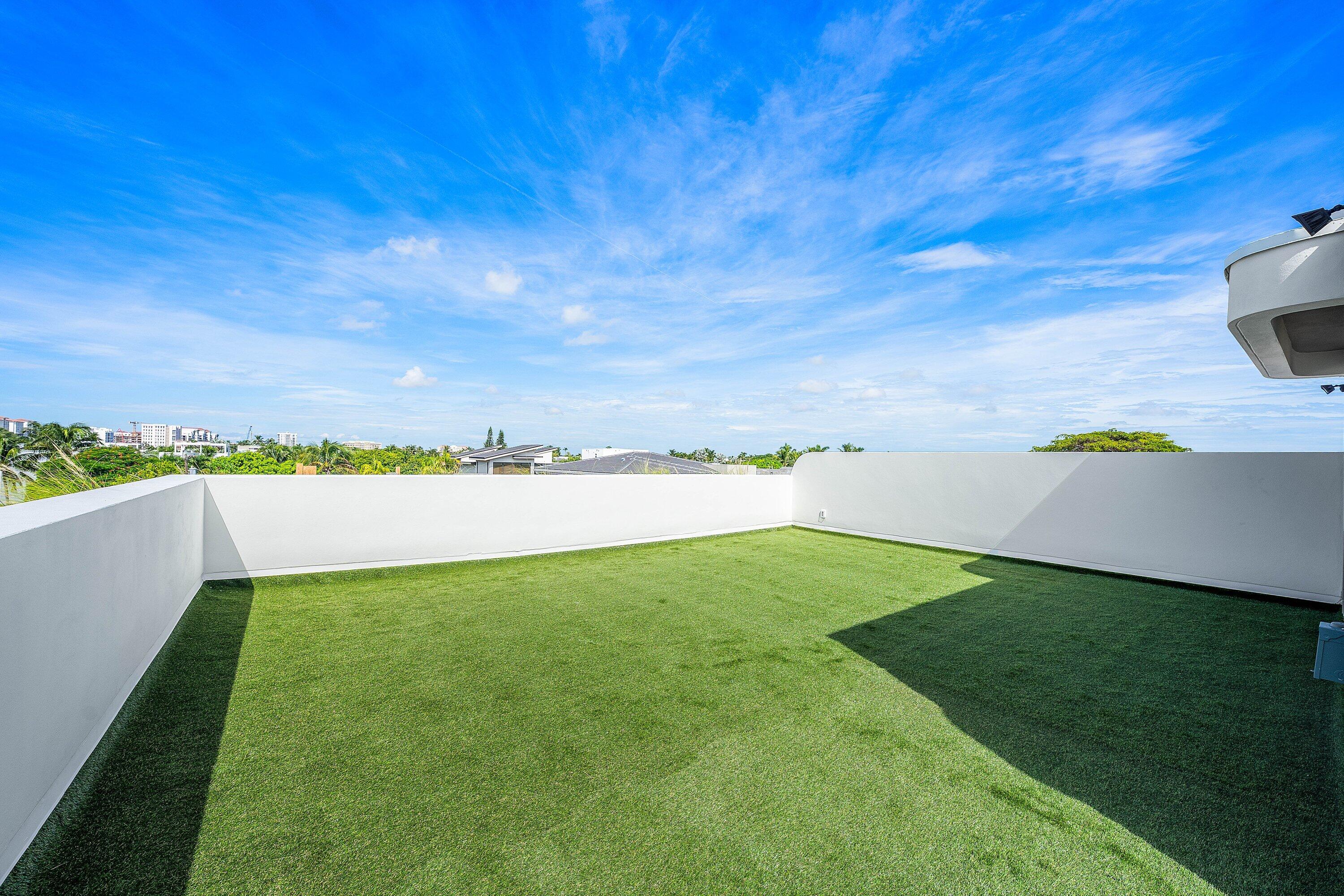 Rooftop terrace with a green lawn, white walls, and distant city buildings.