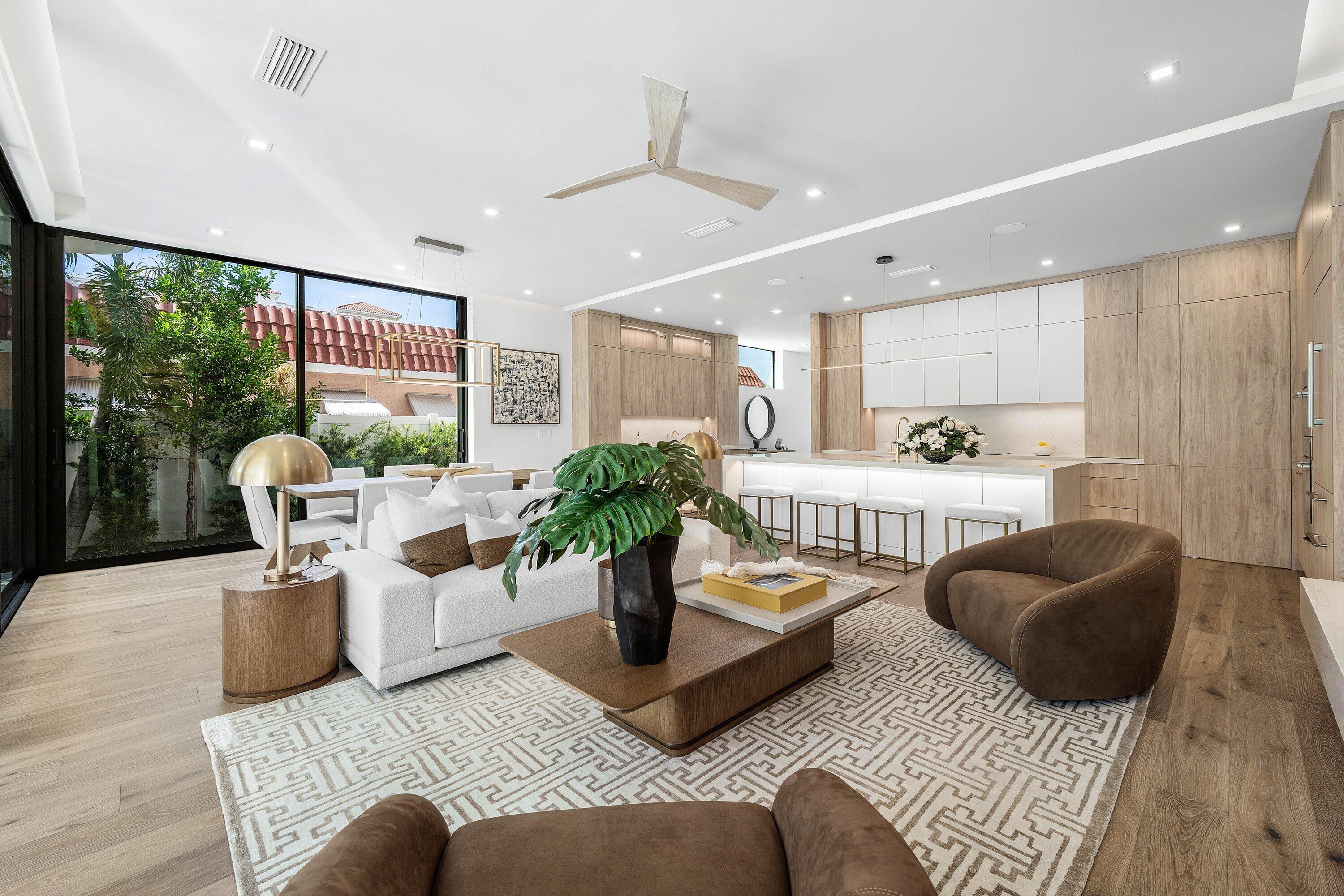 Open-plan living room with a white sofa, patterned rug, and kitchen island beside glass doors.