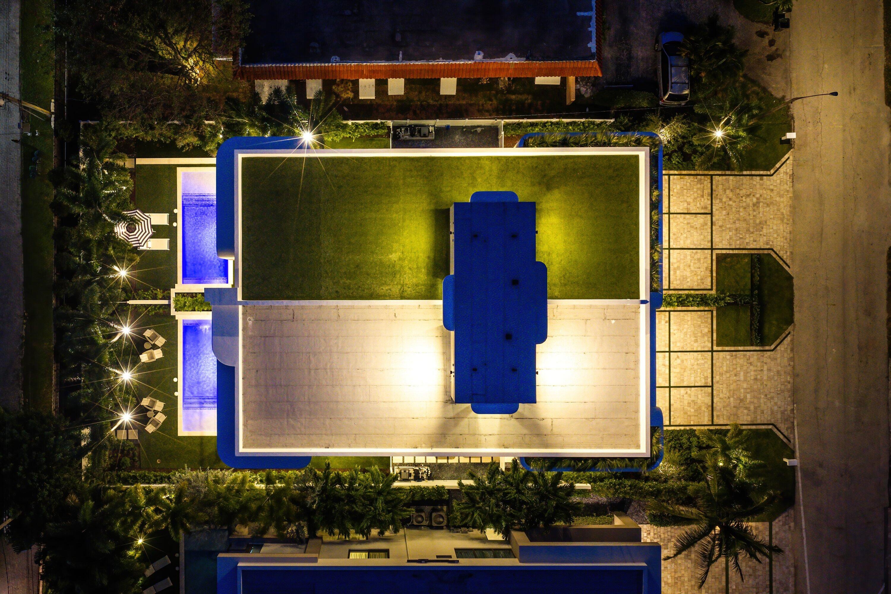 Aerial view of a flat-roofed home and illuminated pool at night.