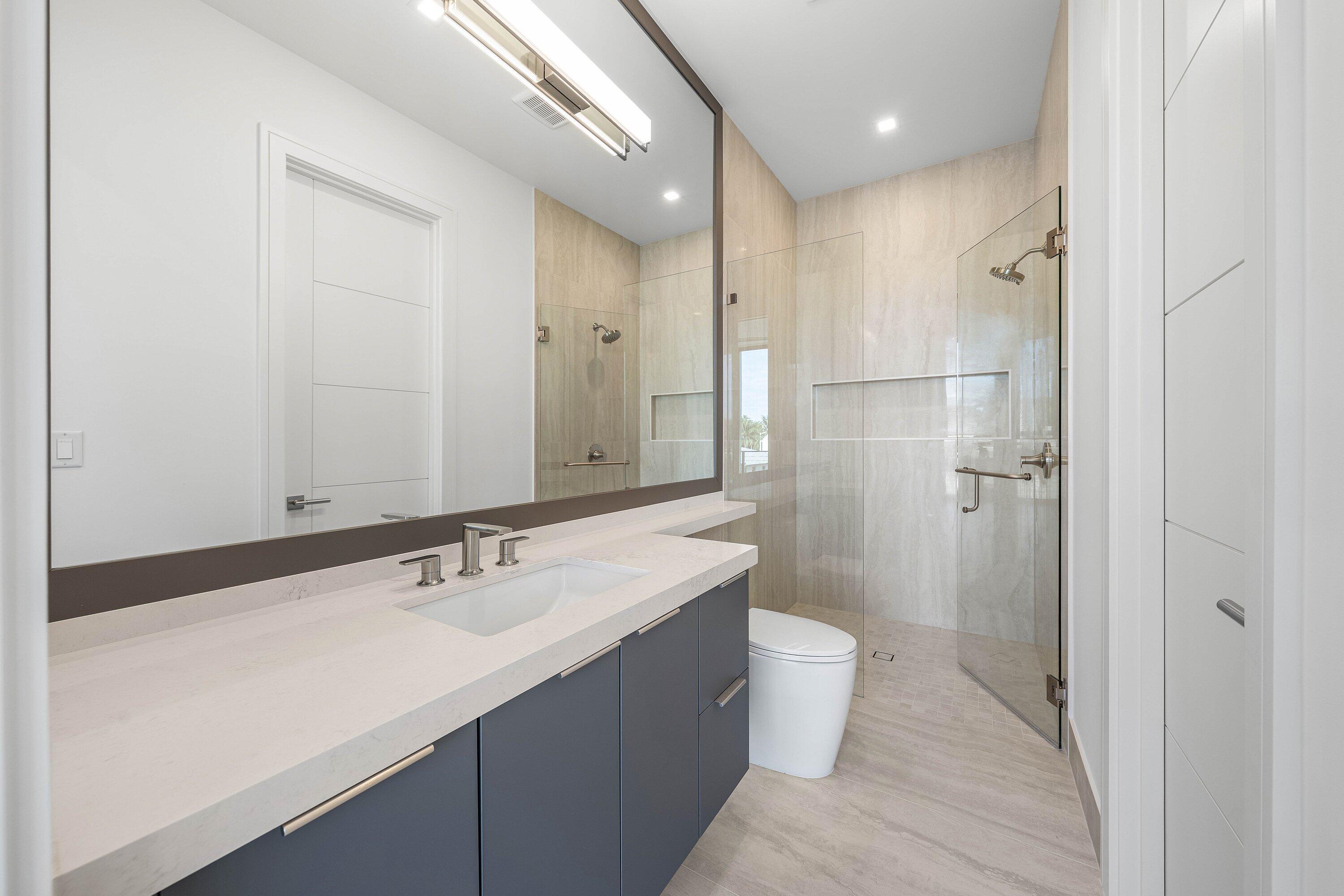Modern bathroom with a long gray vanity and a glass-enclosed walk-in shower.