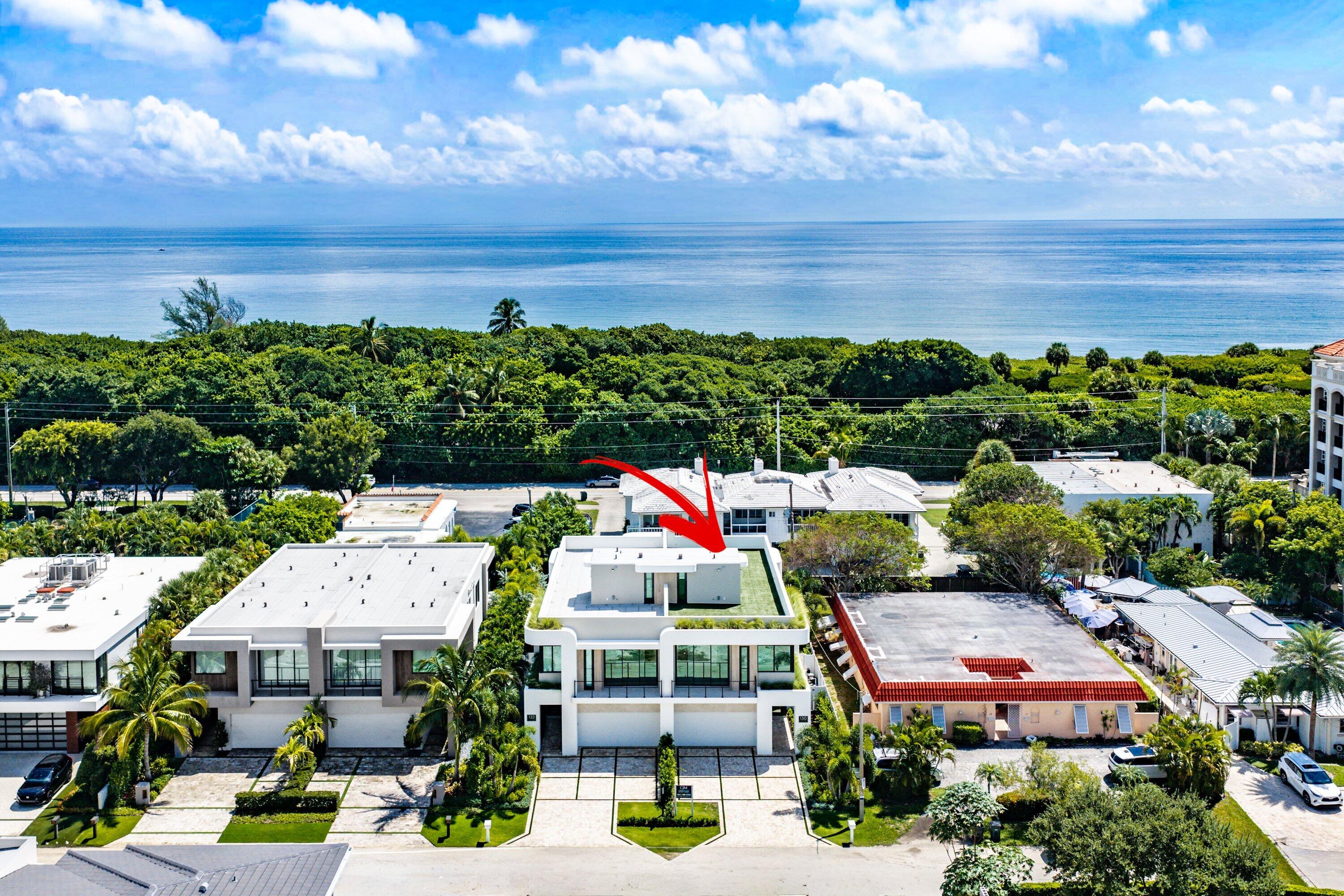 Aerial view of the white modern home, marked by a red arrow, with the ocean beyond.
