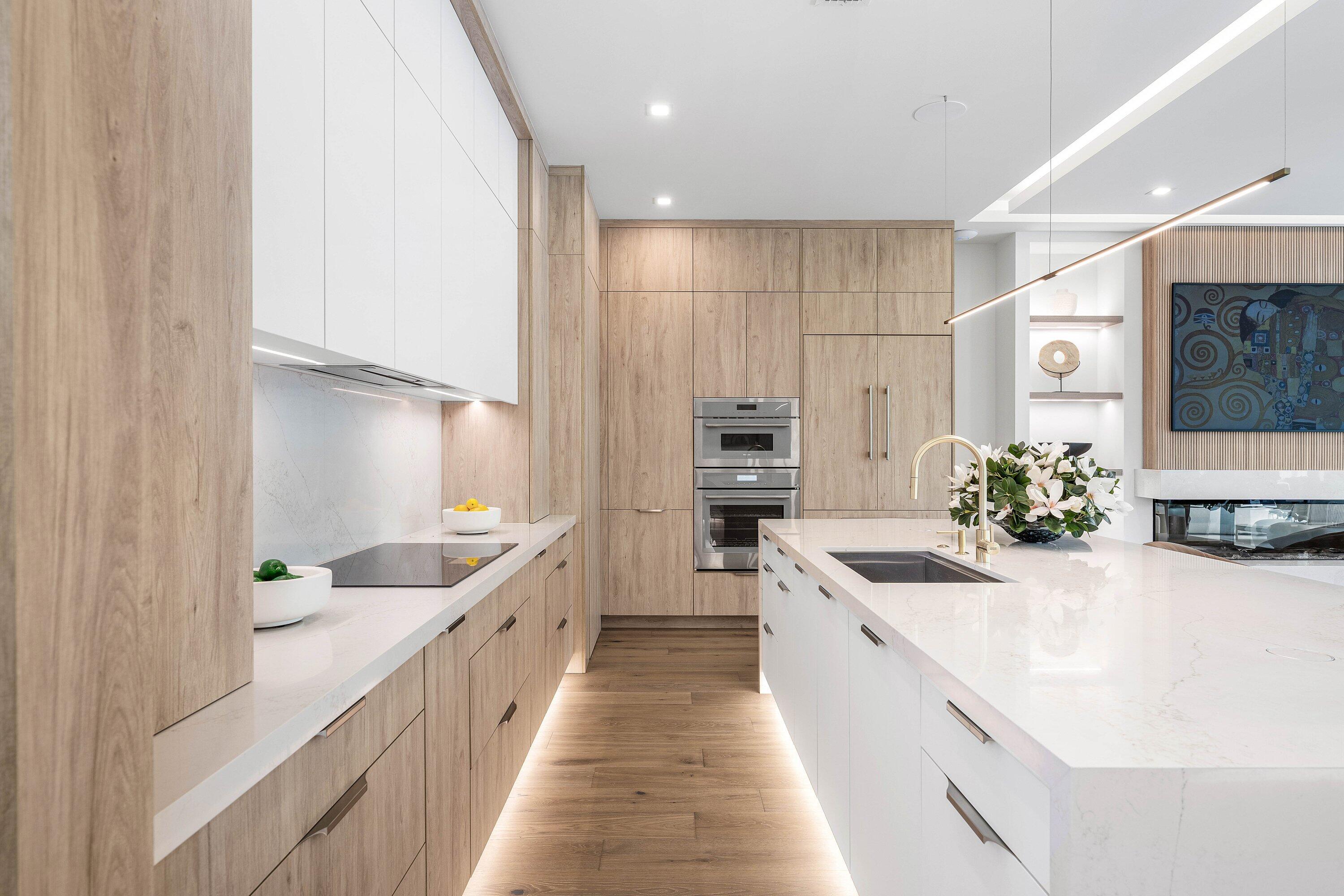 Modern kitchen with pale wood cabinetry, a large white island, and stacked stainless steel ovens.