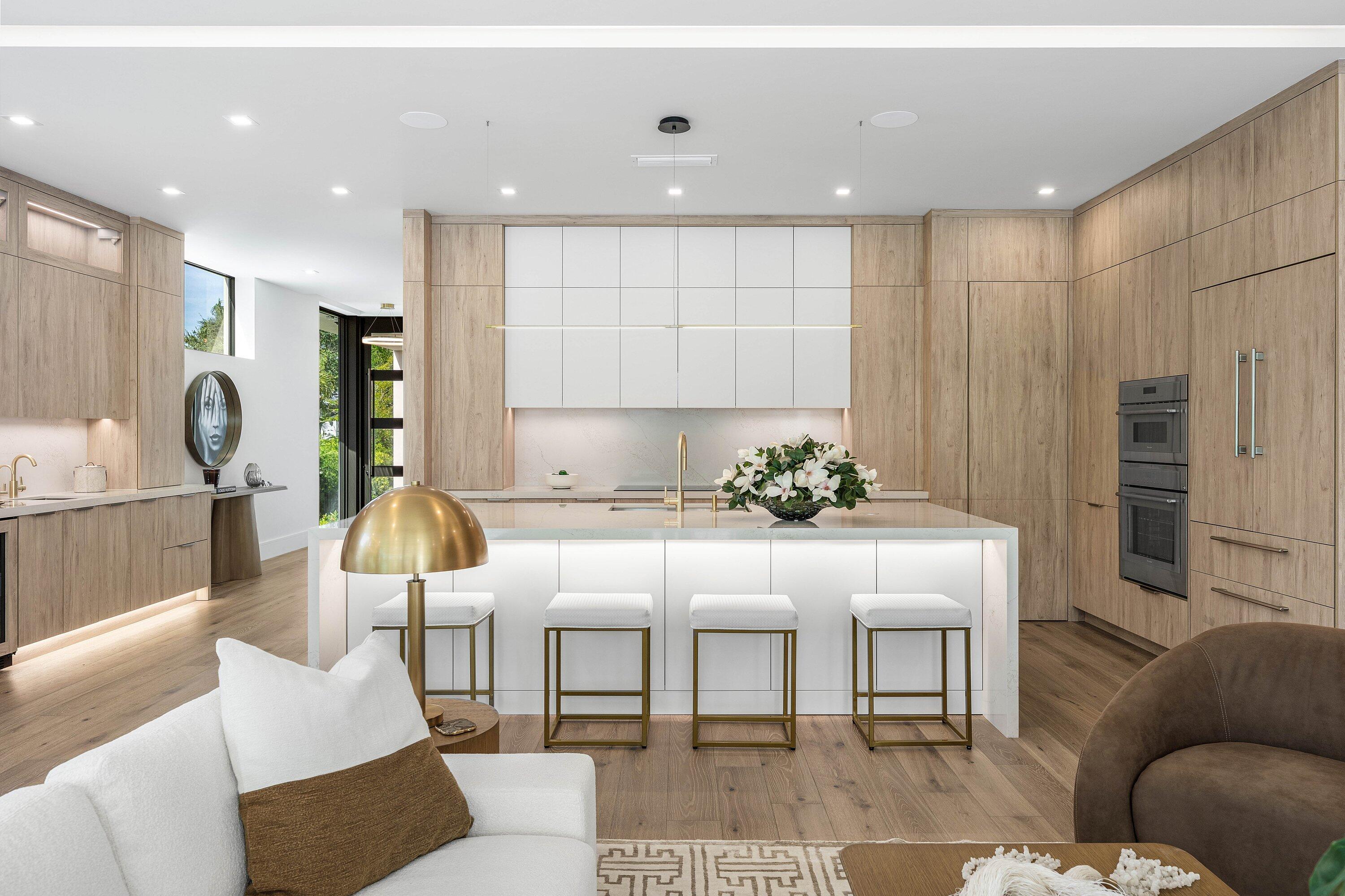 Modern kitchen with a white island, four brass-framed stools, and light wood cabinetry