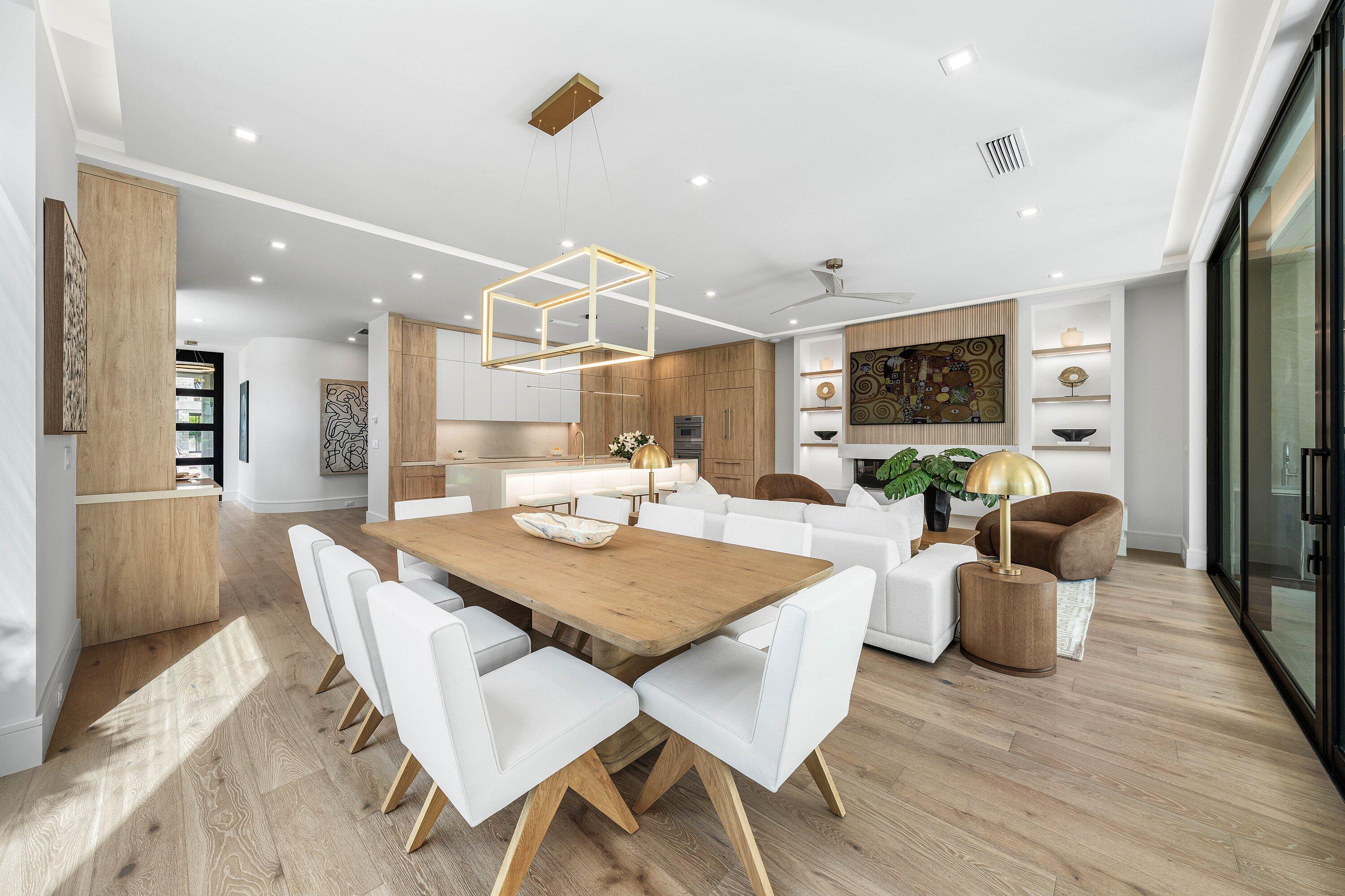 Open-plan dining room with a wood table, white chairs, and modern kitchen.