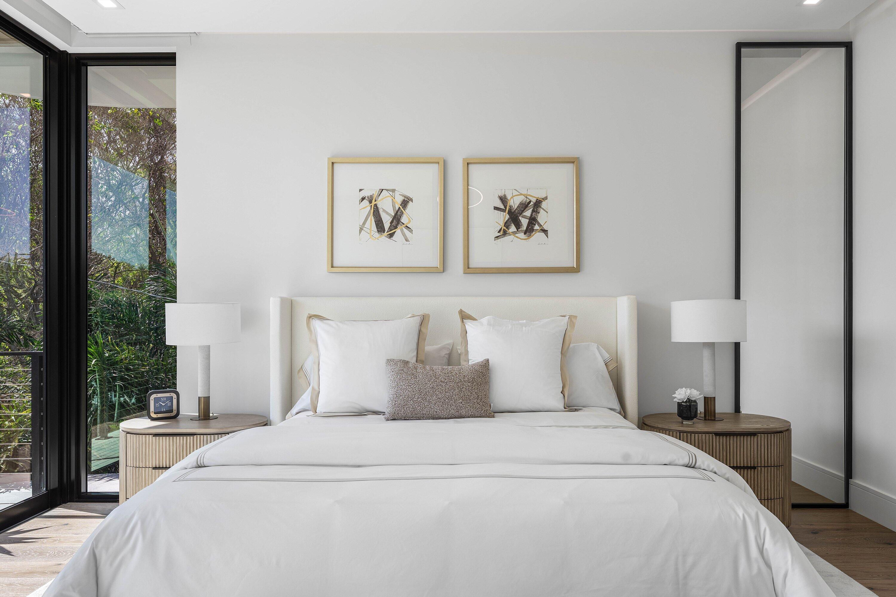 Furnished bedroom with a white bed and glass doors overlooking greenery.