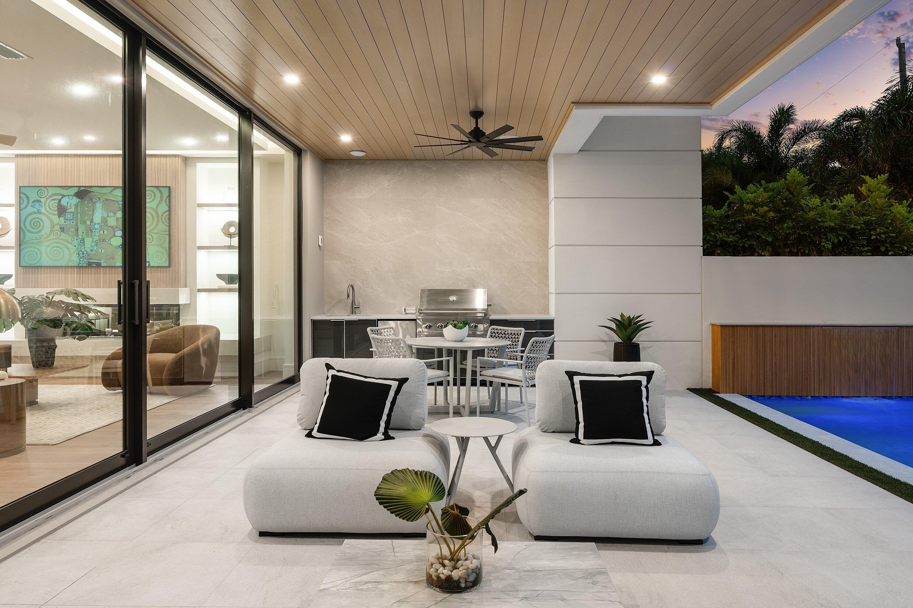 Covered patio with modern lounge seating, an outdoor kitchen, and a pool at dusk.