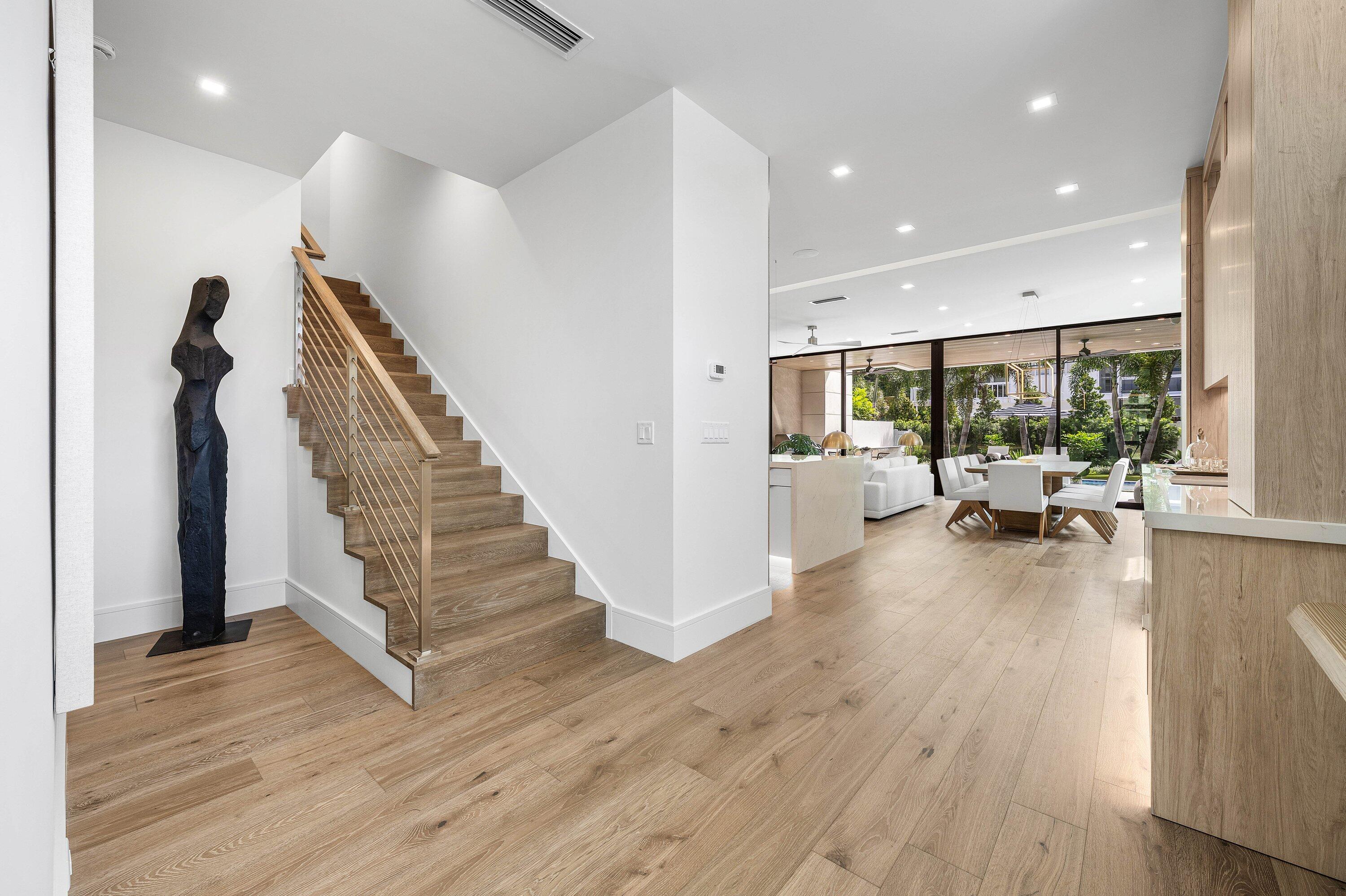 Modern foyer with a wood staircase, wide-plank floors, and an open dining area overlooking the garden.