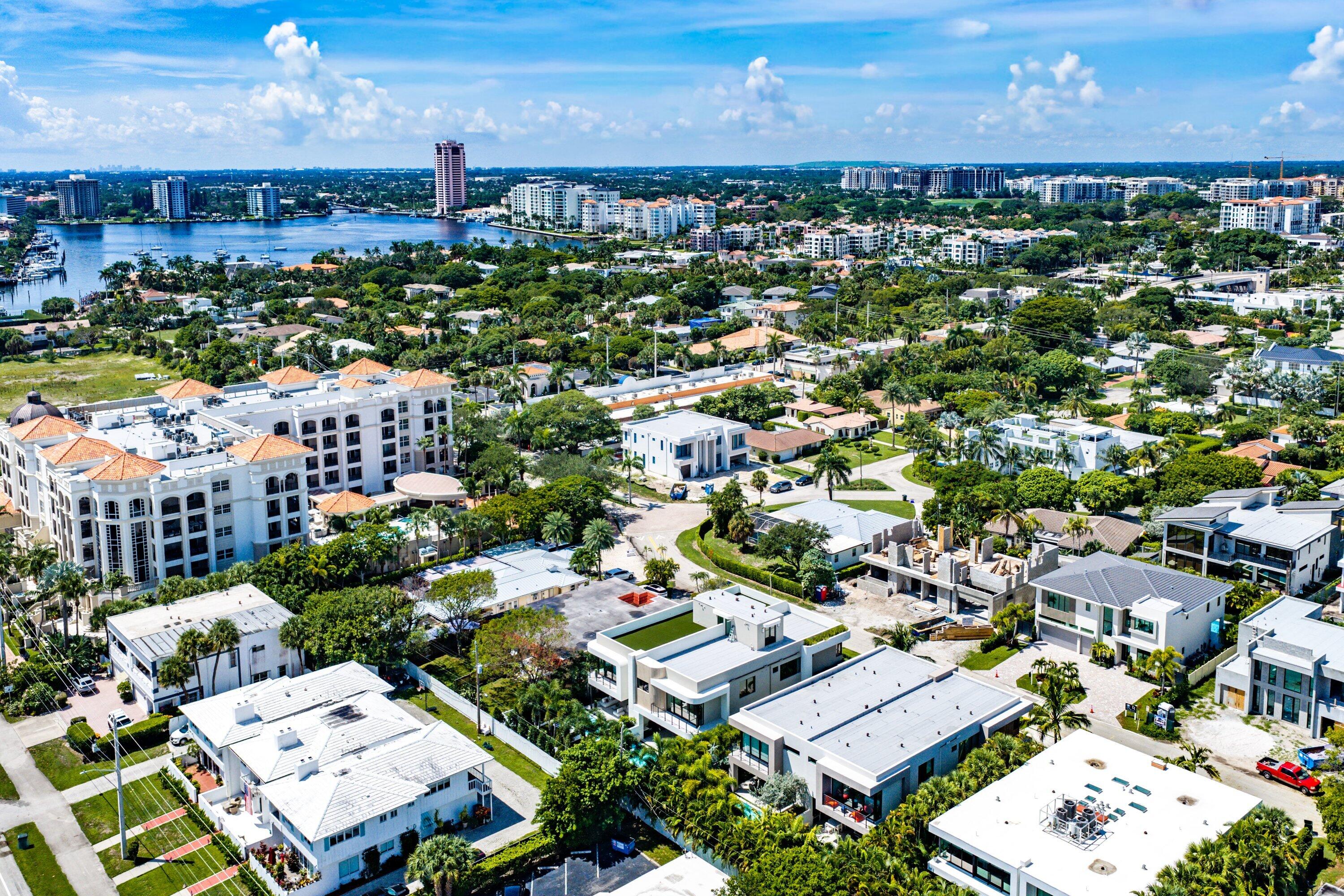Aerial view of modern homes and leafy streets beside a waterfront inlet with boats.