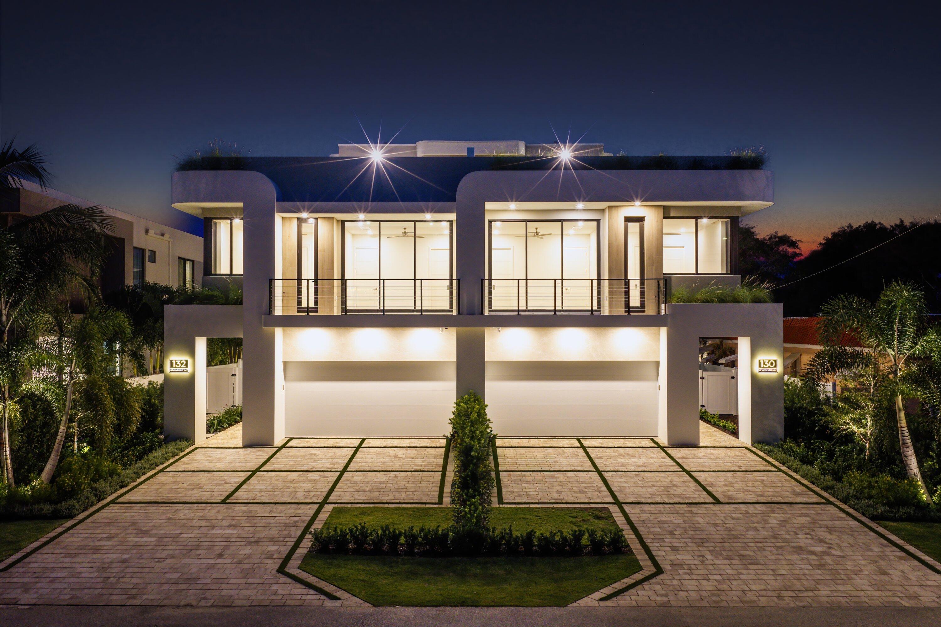 Modern two-story home at dusk with a glass-fronted balcony, double garage, and paved driveway.