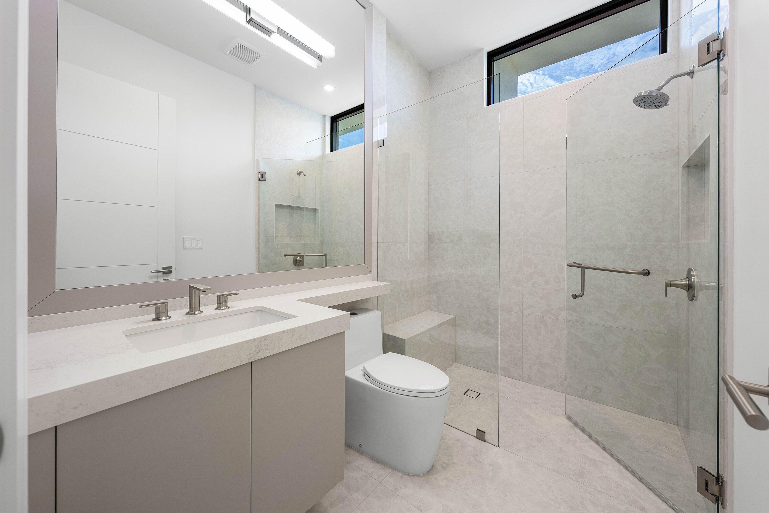 Modern bathroom with a wide vanity and glass-enclosed walk-in shower beneath a high window.