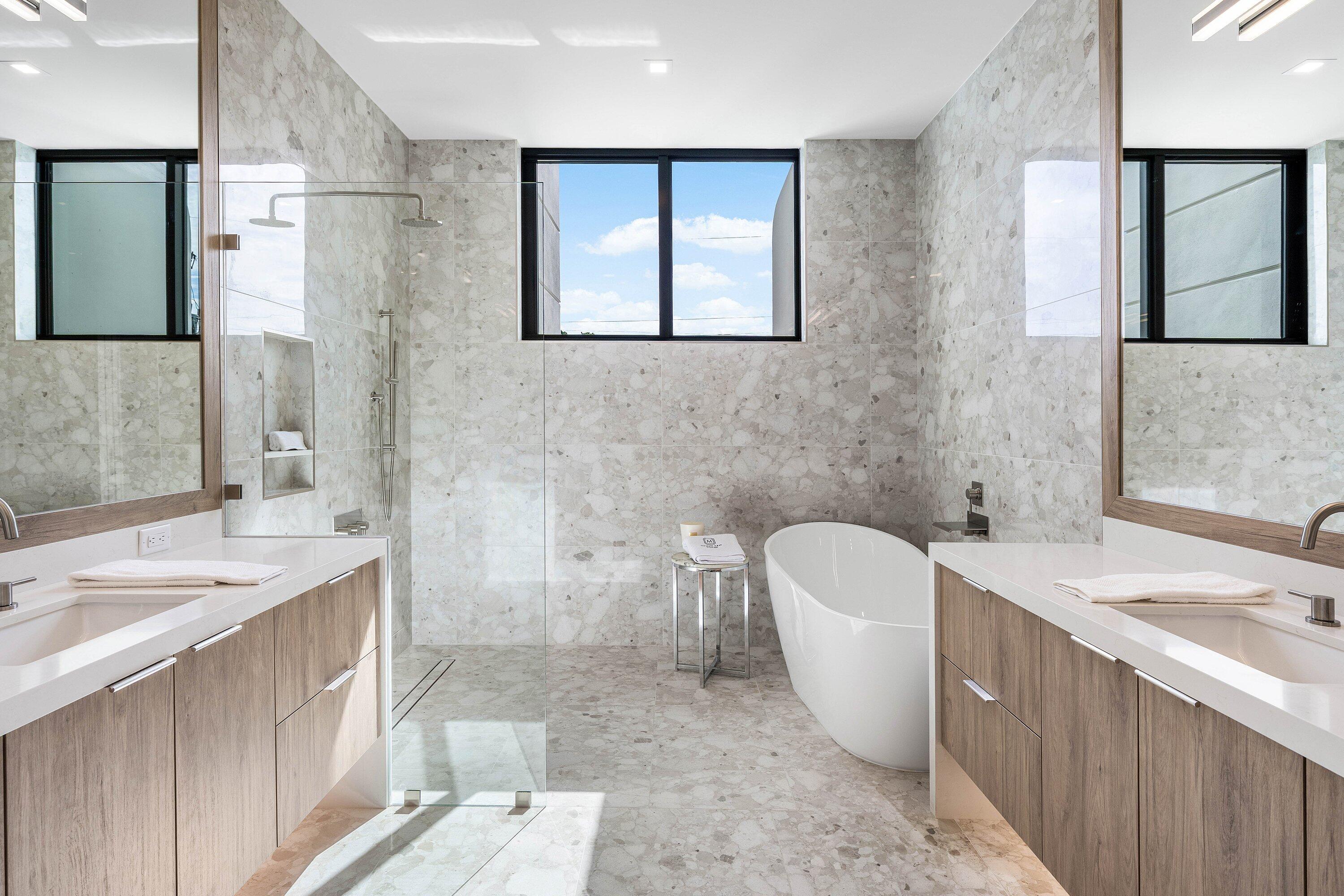 Modern bathroom with dual wood vanities, a glass shower, and a freestanding tub.