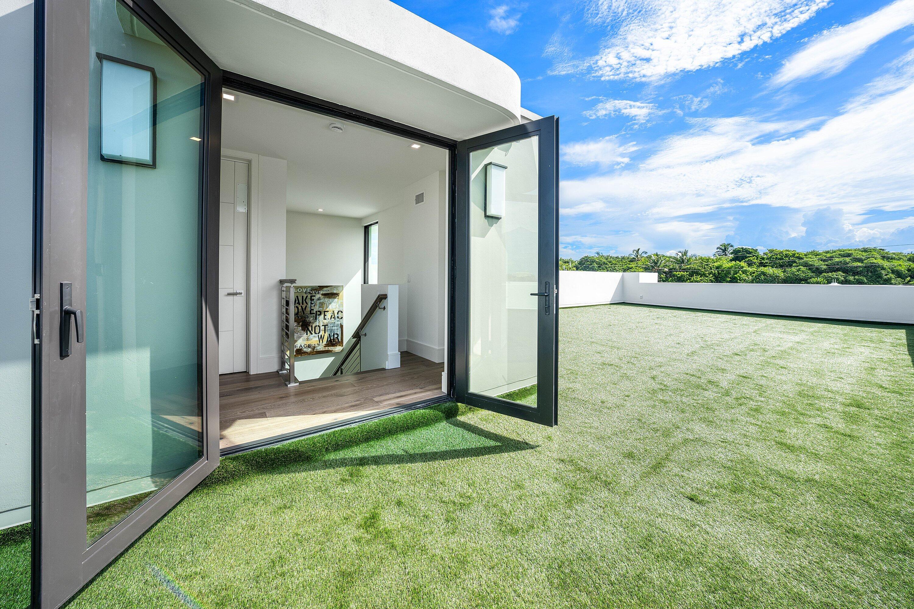 Rooftop terrace with artificial turf beside open glass doors leading into a modern home.