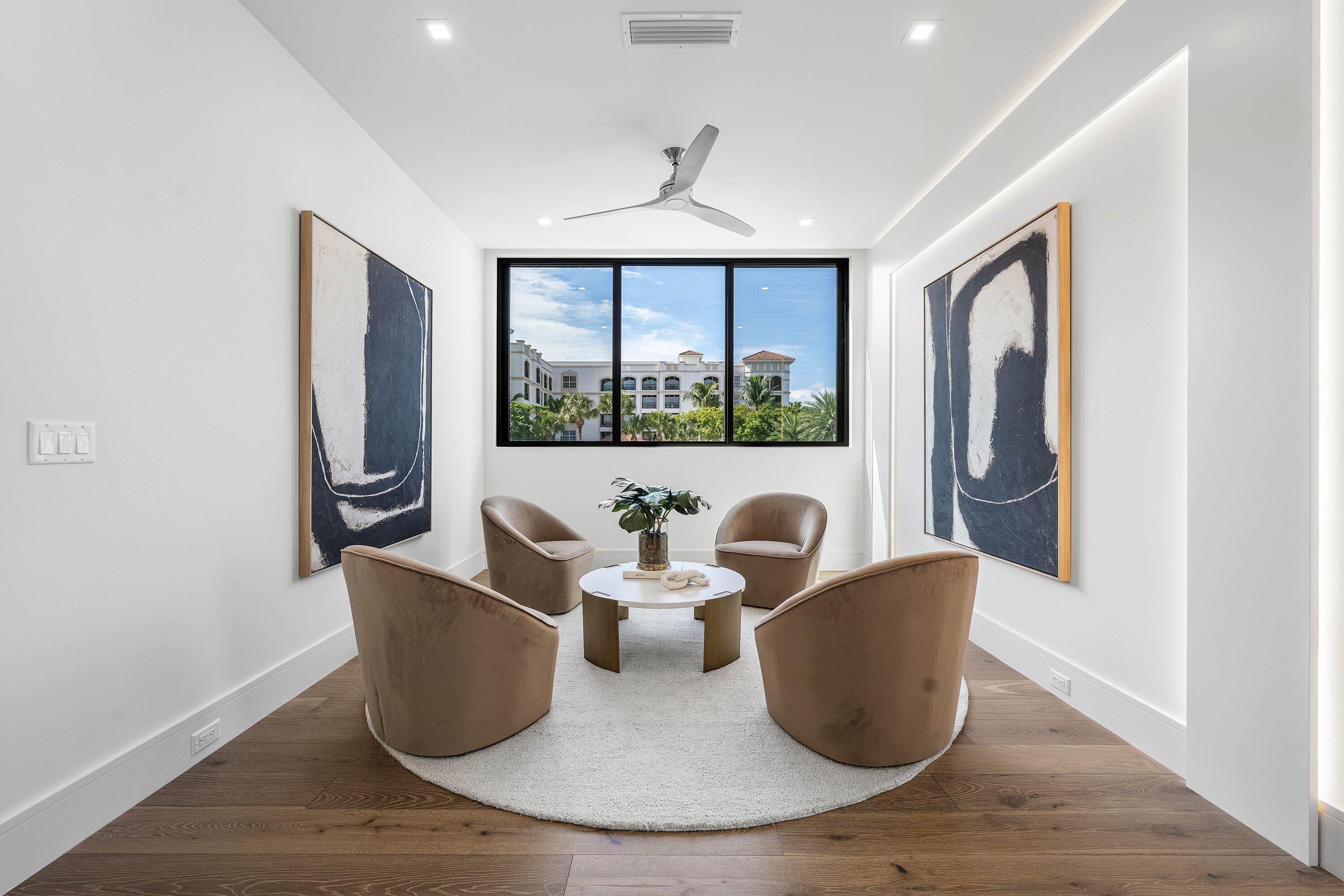 Modern sitting room with four tan chairs, abstract art, and a wide window overlooking greenery.