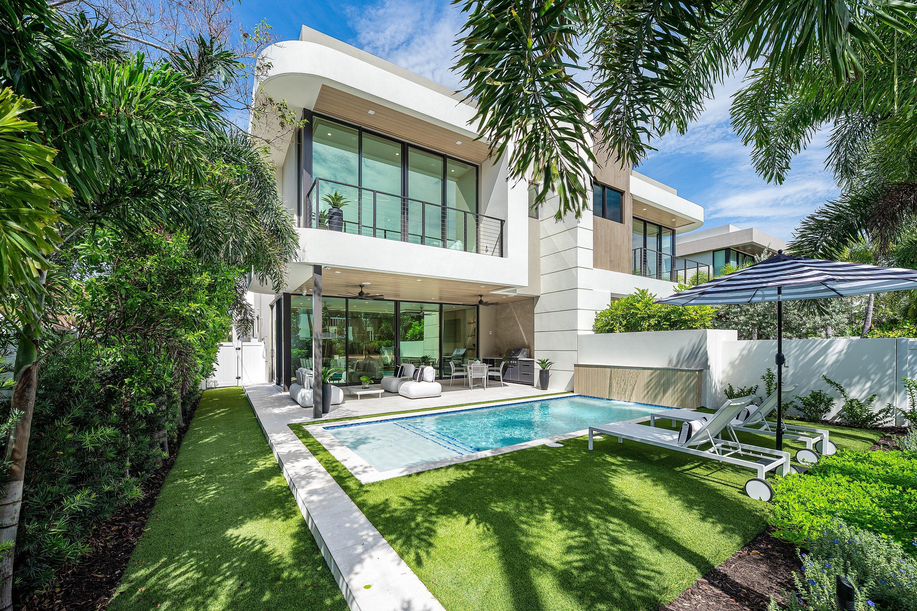 Modern two-story home with a backyard pool, furnished patio, and tropical landscaping.