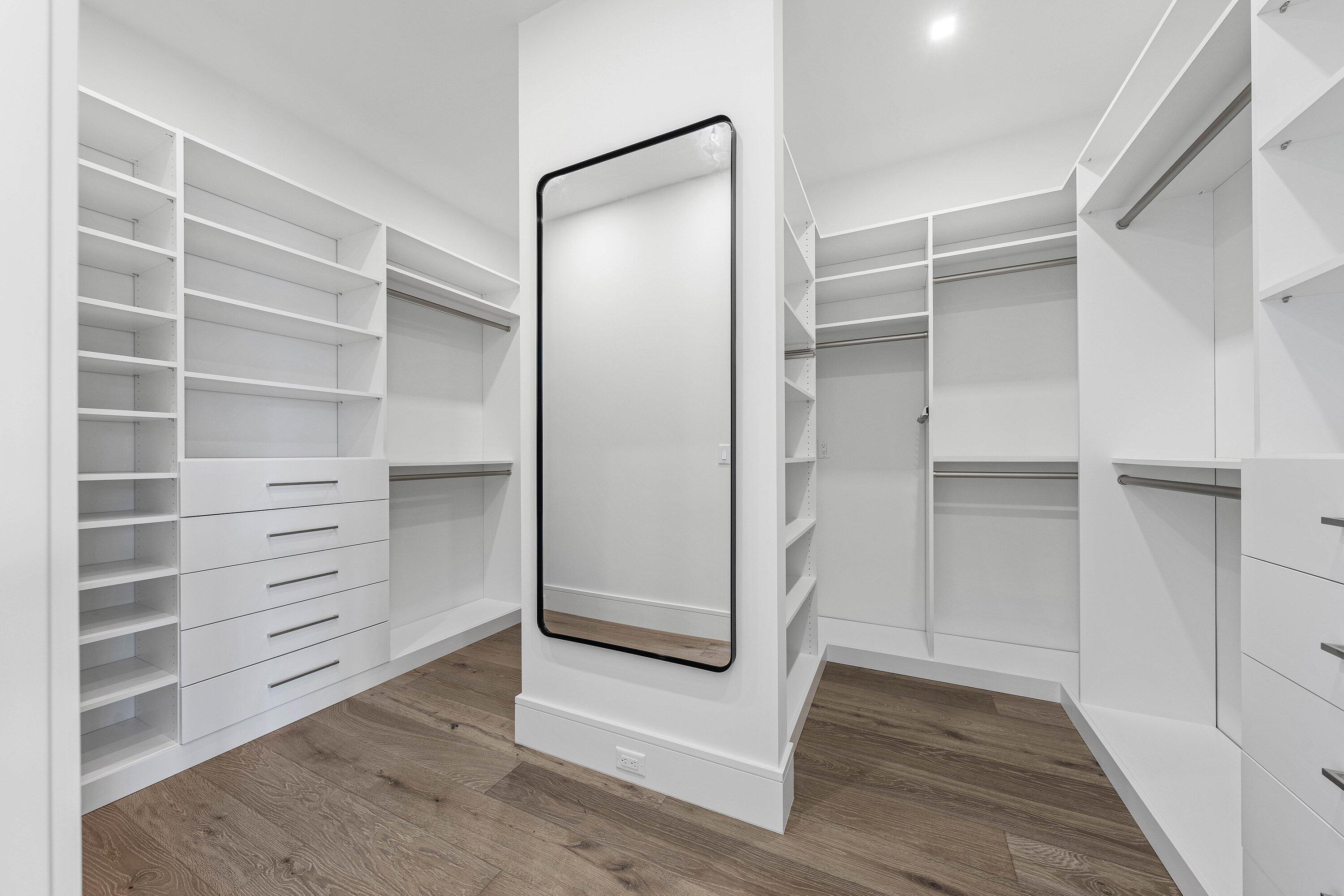 Walk-in closet with extensive white built-in storage, a full-length mirror, and wood flooring.