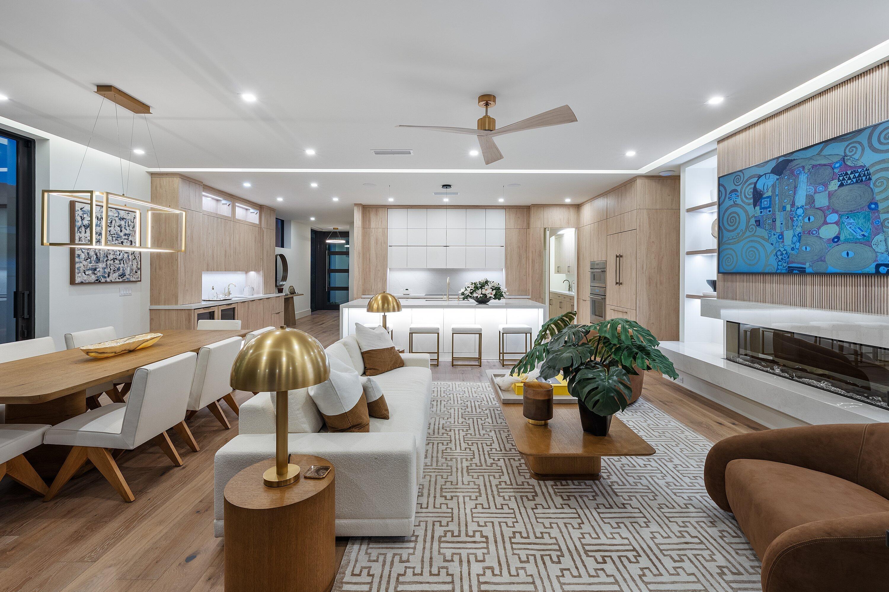 Open-plan living room and kitchen with light wood cabinetry, white sofas, and a long fireplace.