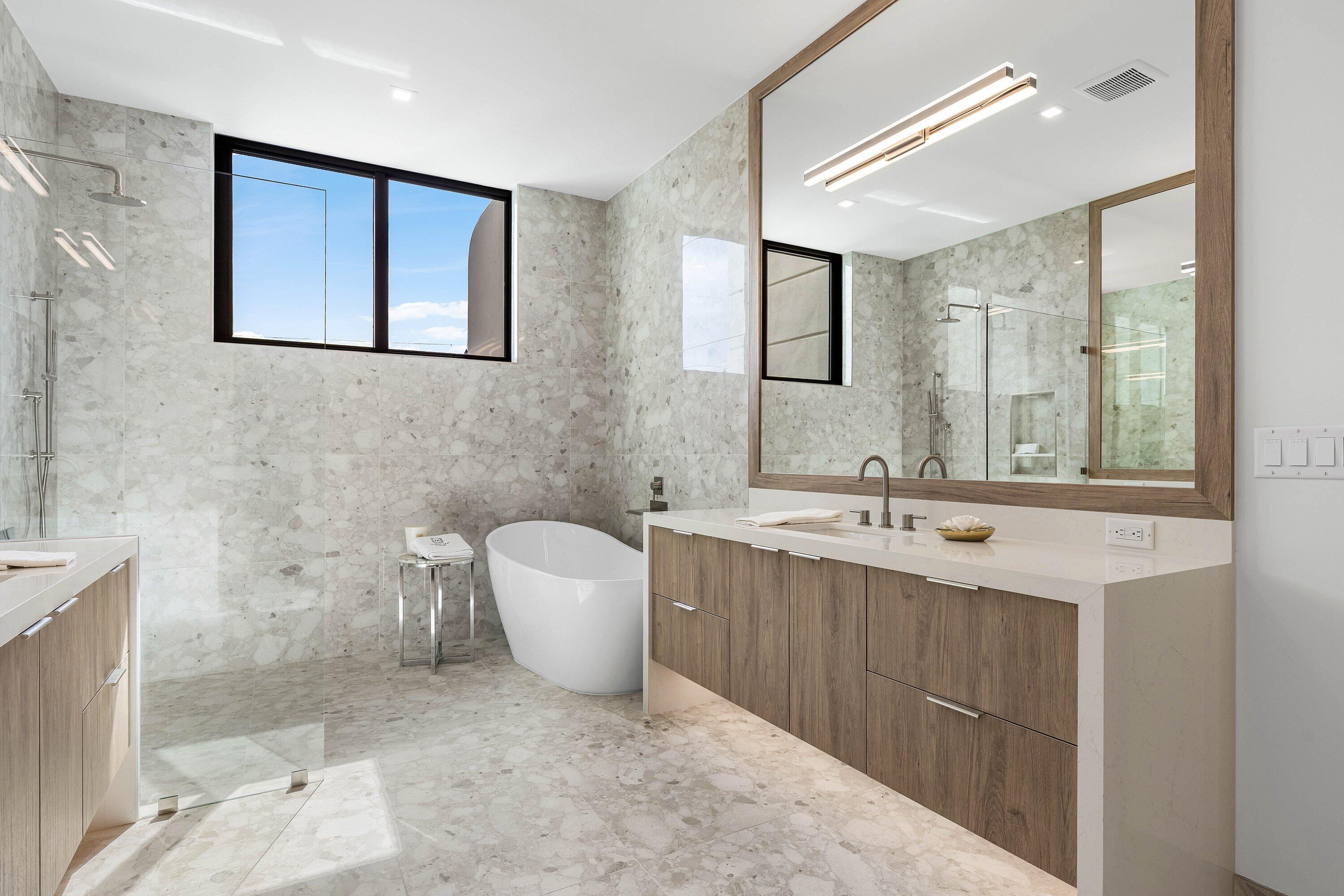 Modern stone-tiled bathroom with a freestanding tub, glass shower, and wood vanity.