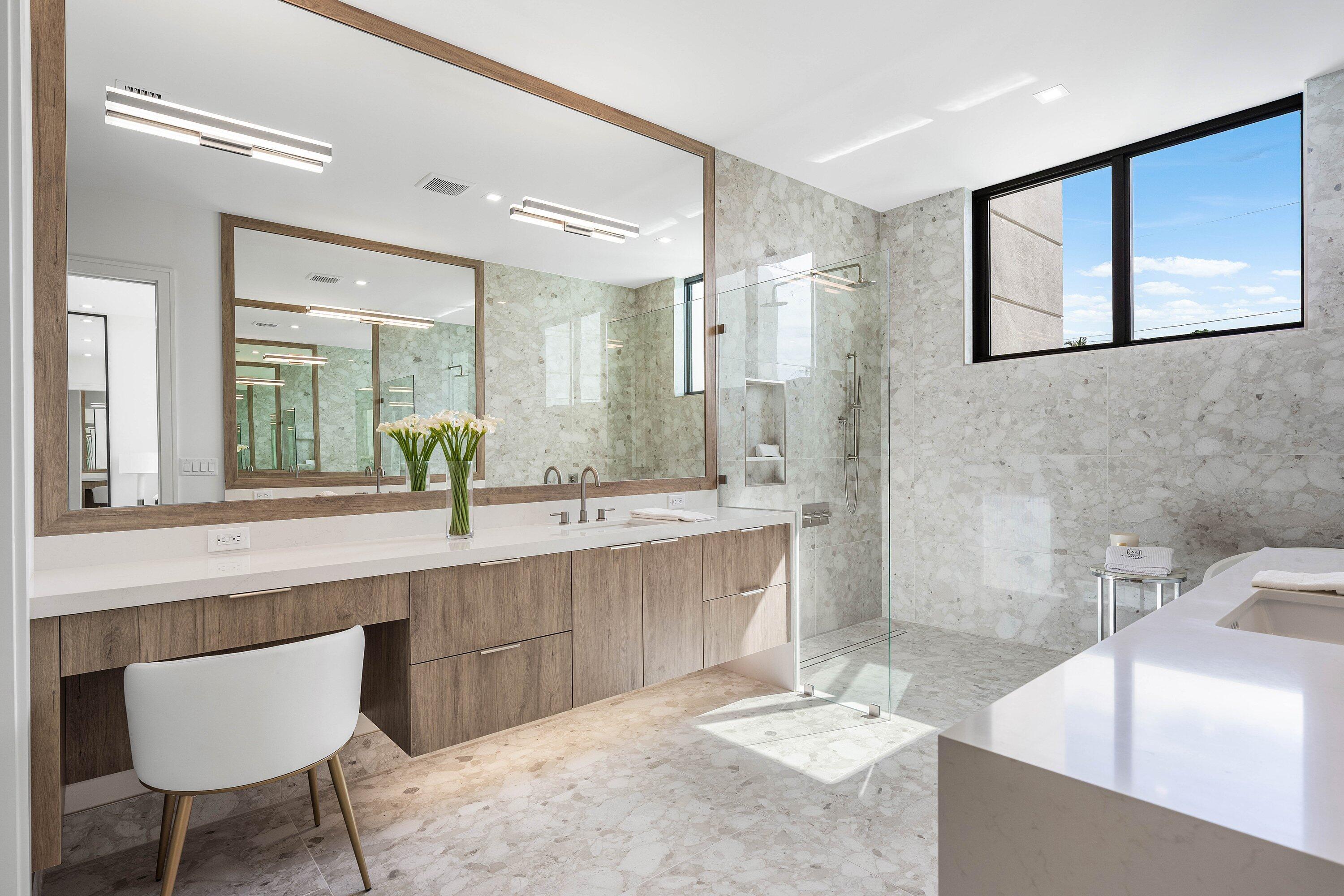 Modern bathroom with a wood-front vanity, pale stone tile, and glass-enclosed shower.