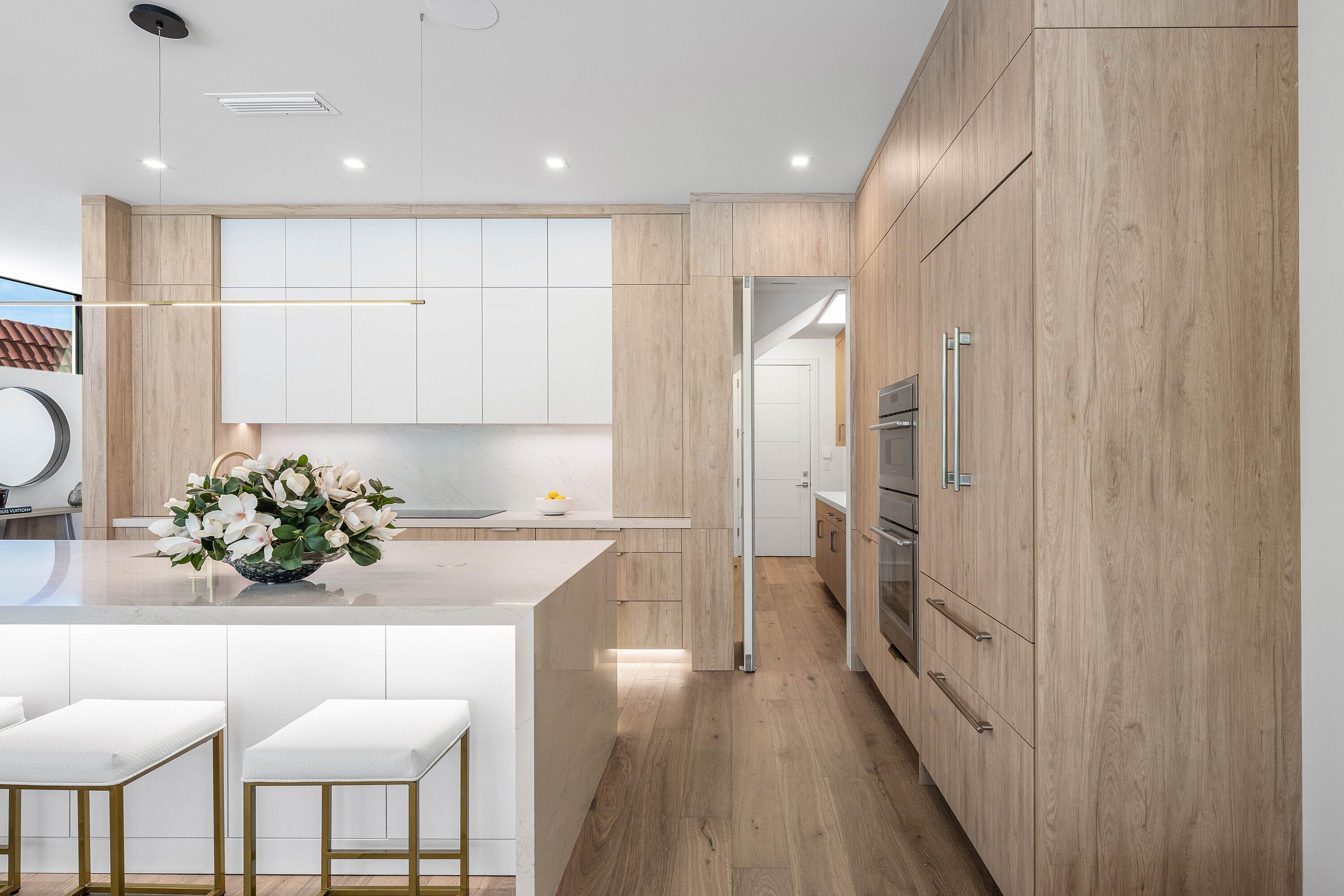 Modern kitchen with light wood cabinets, a white stone island, and built-in double ovens.