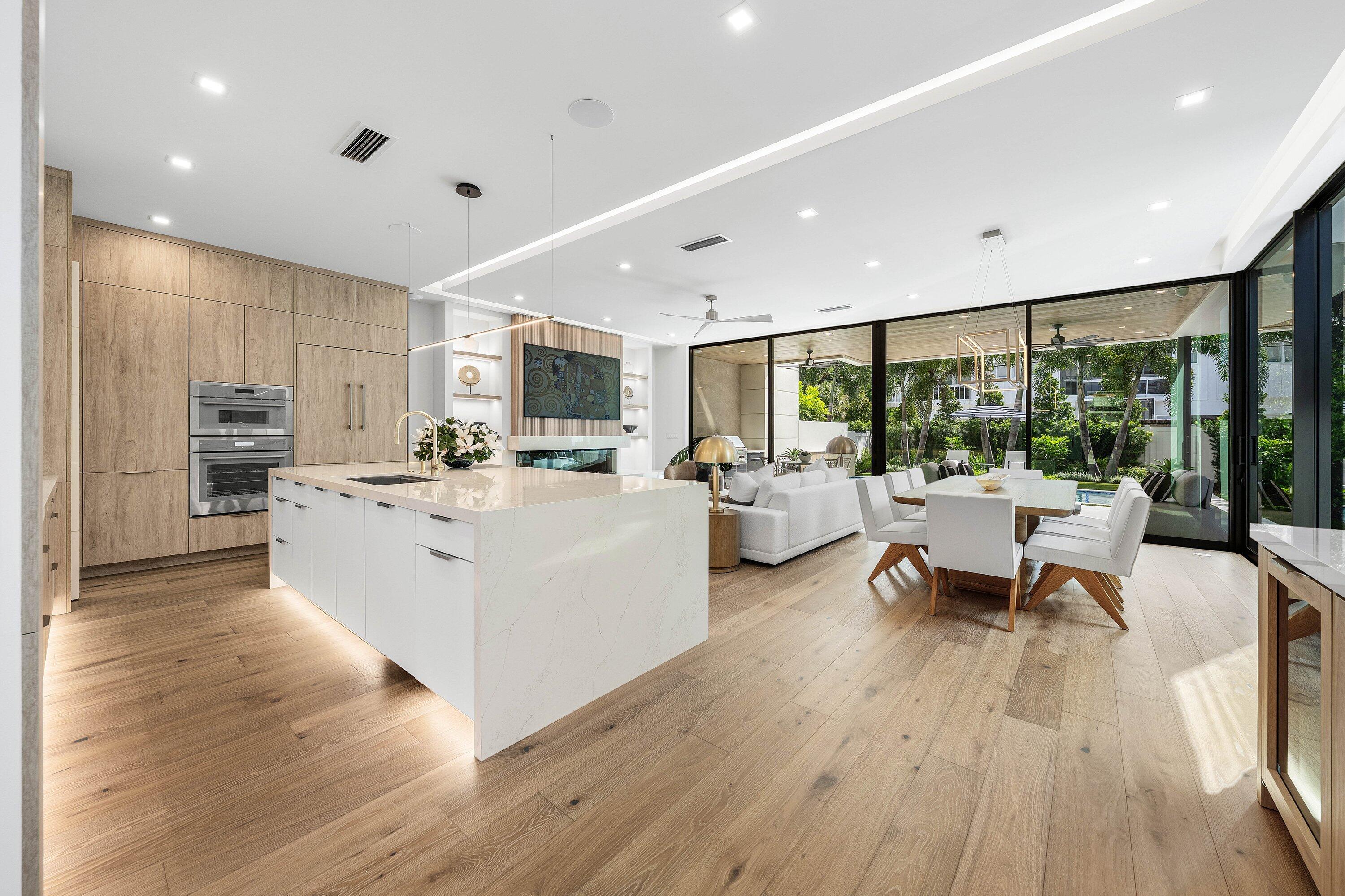 Open-plan kitchen with a large white island, wood cabinetry, and glass doors facing the garden.