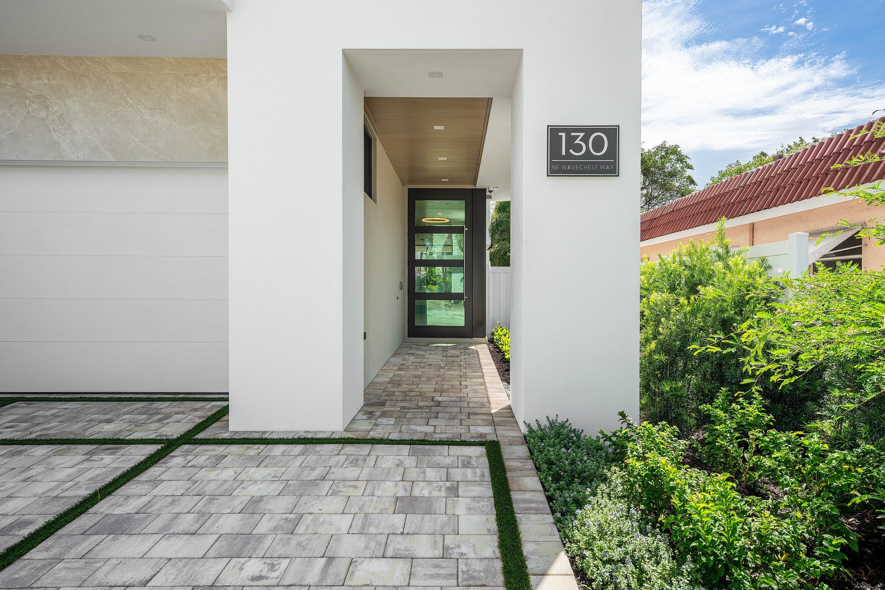 Modern home entrance with a covered walkway, dark glass door, and stone-paver path.
