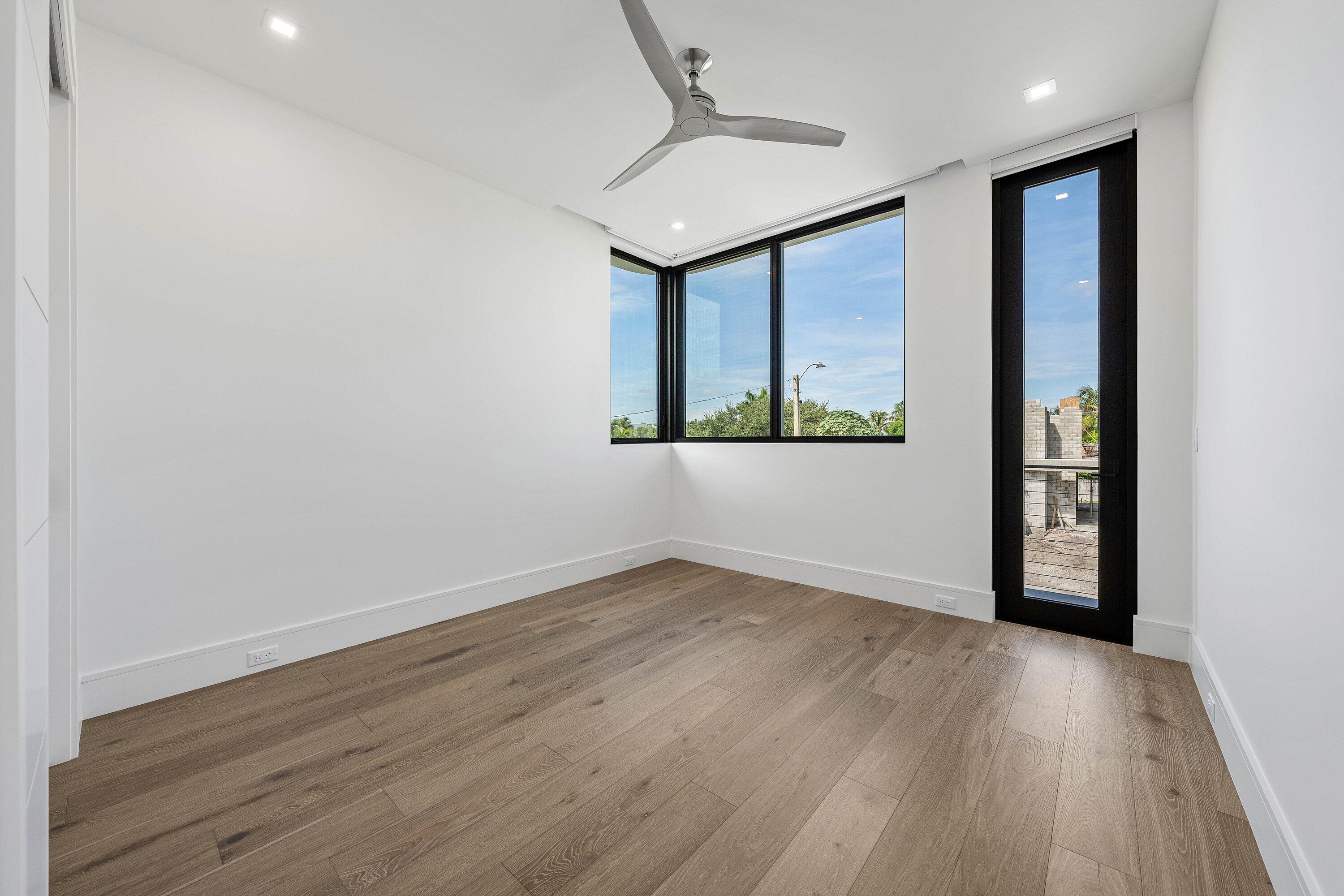 Empty room with wood floors, a ceiling fan, and black-framed windows and glass door.
