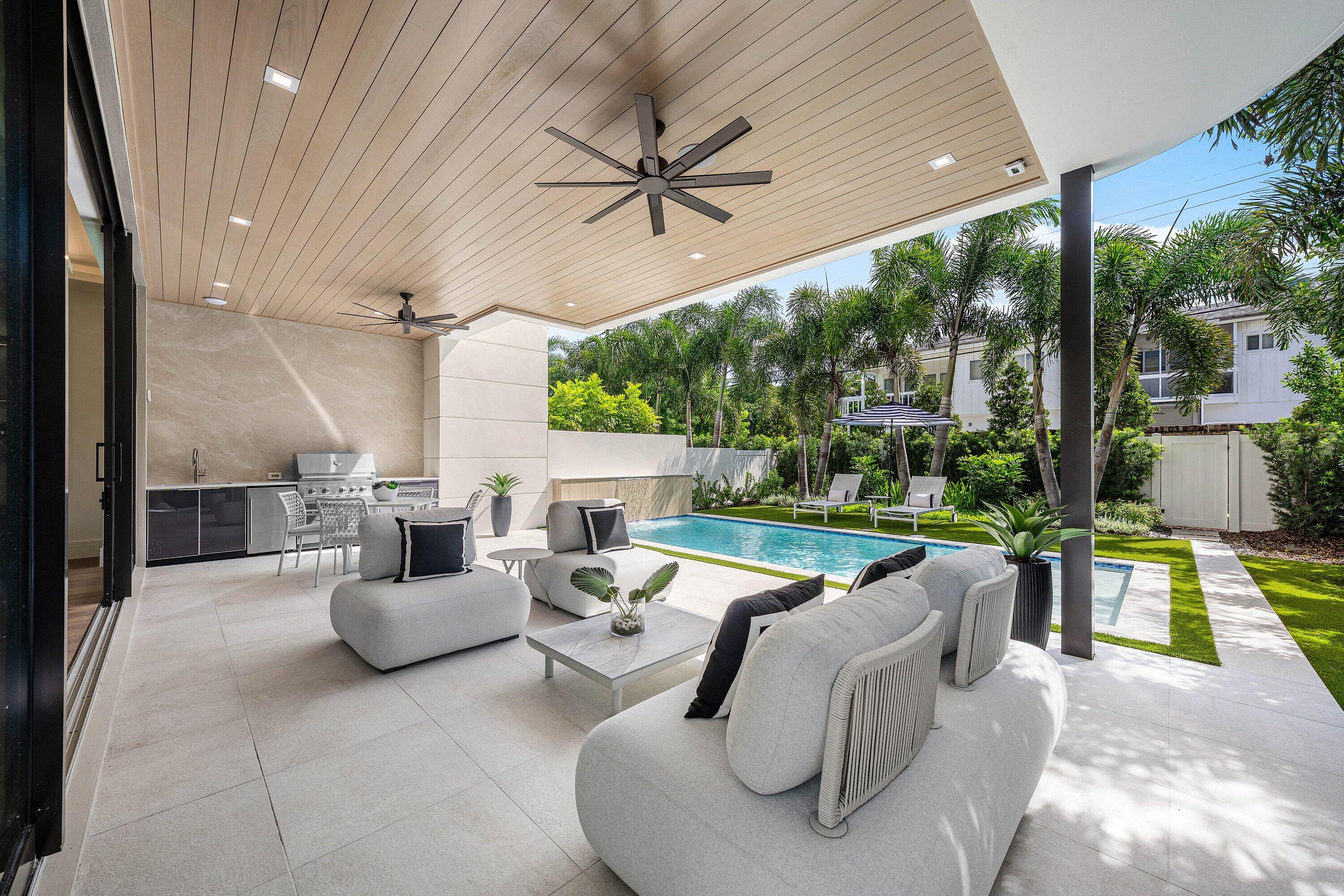 Covered patio with lounge seating and an outdoor kitchen beside a landscaped swimming pool.