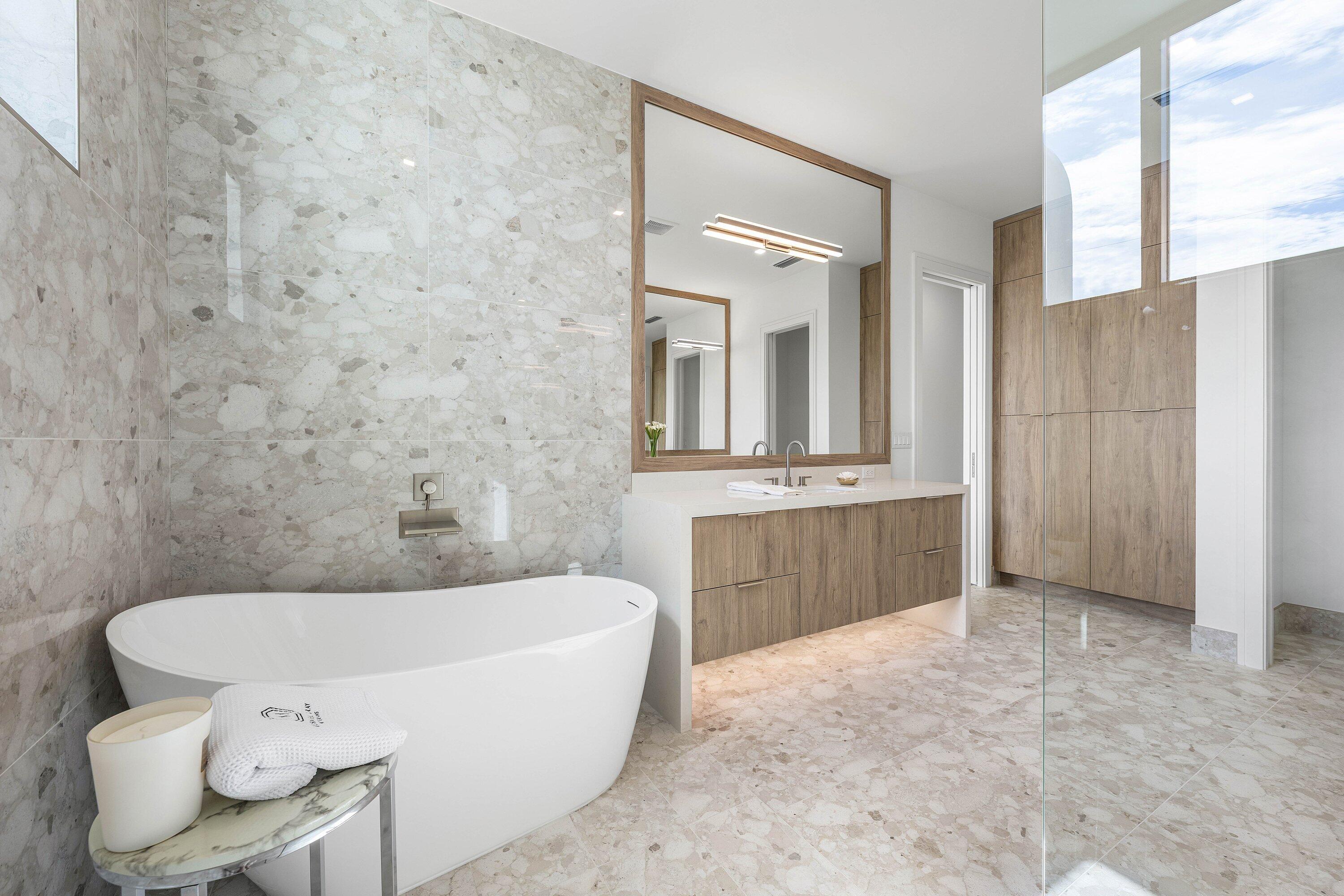 Modern bathroom with a freestanding soaking tub, stone tile, and wood-front vanity.