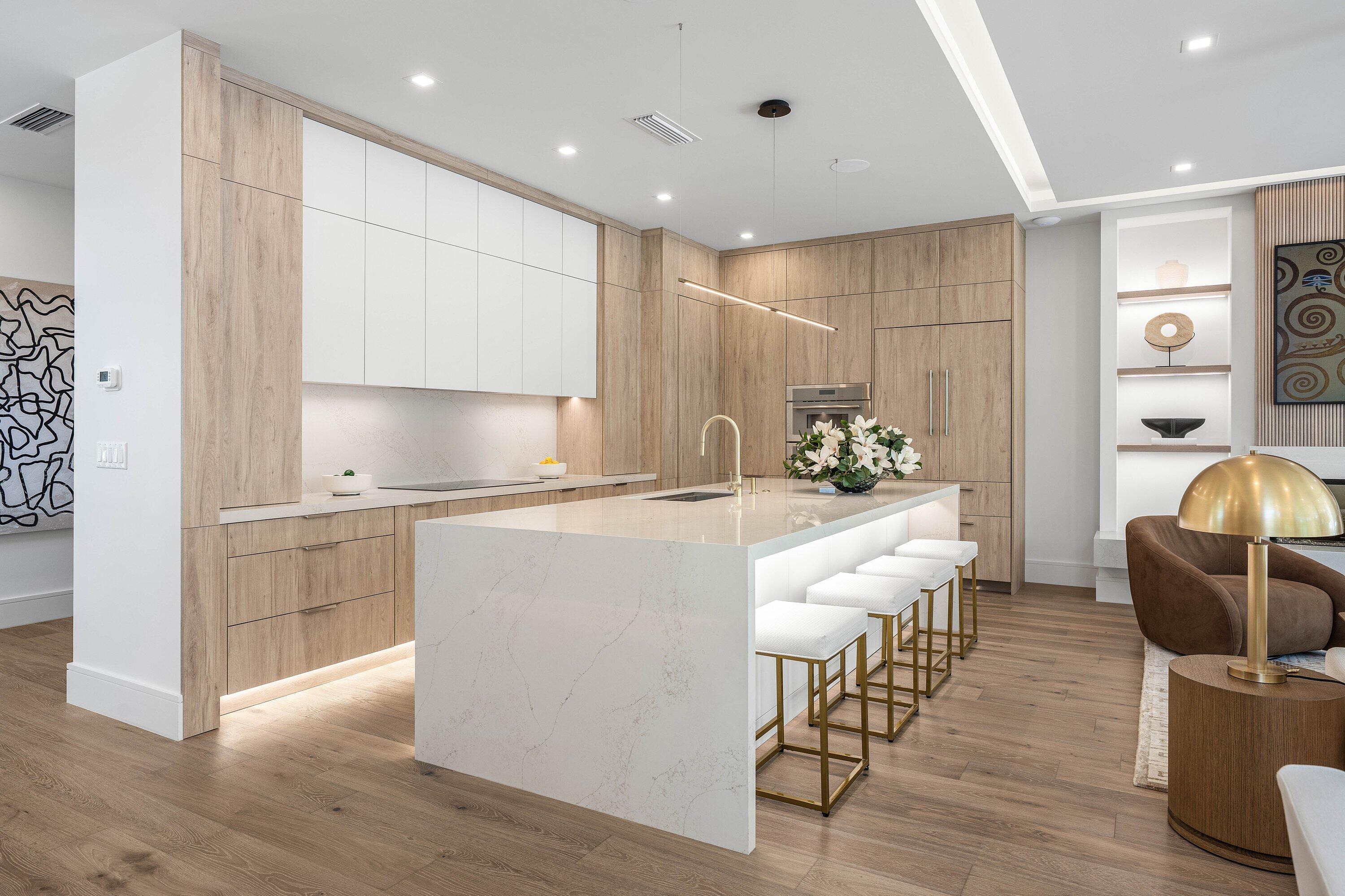 Modern kitchen with a large white stone island, light wood cabinetry, and four bar stools.