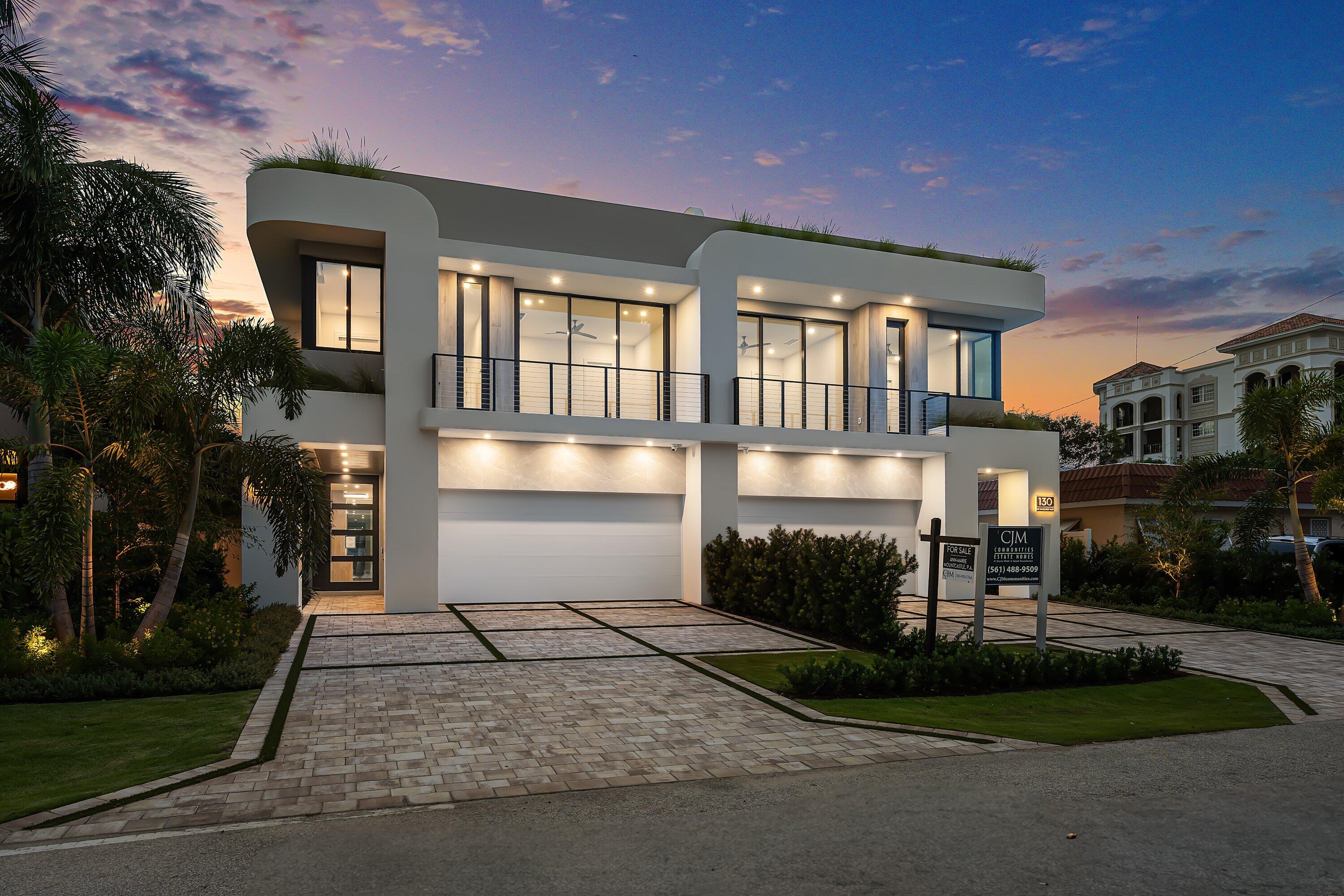 Modern two-story home with curved roof, double garage, and tropical landscaping at dusk.