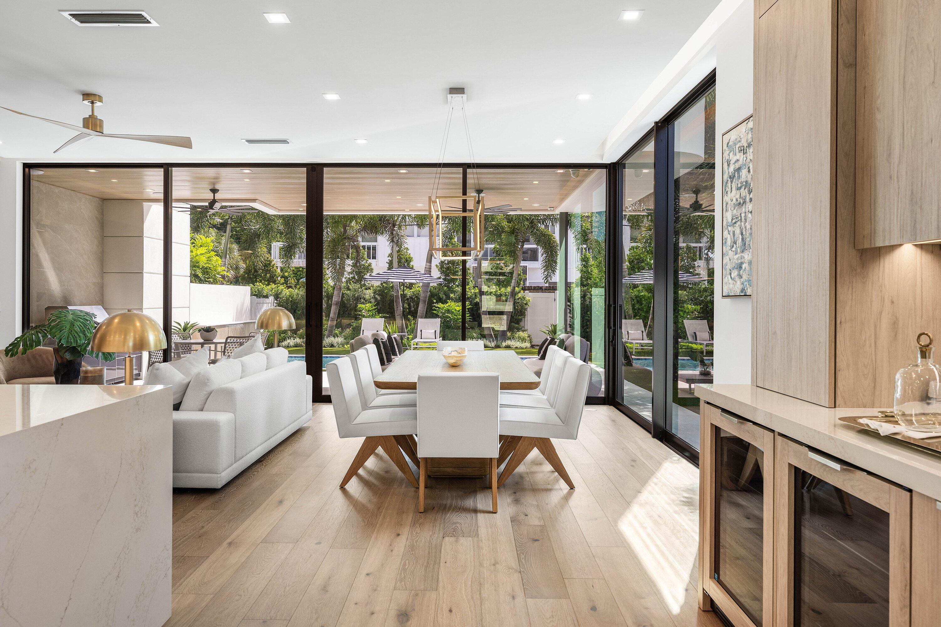 Open-plan dining and living room with floor-to-ceiling glass doors overlooking a pool and garden.