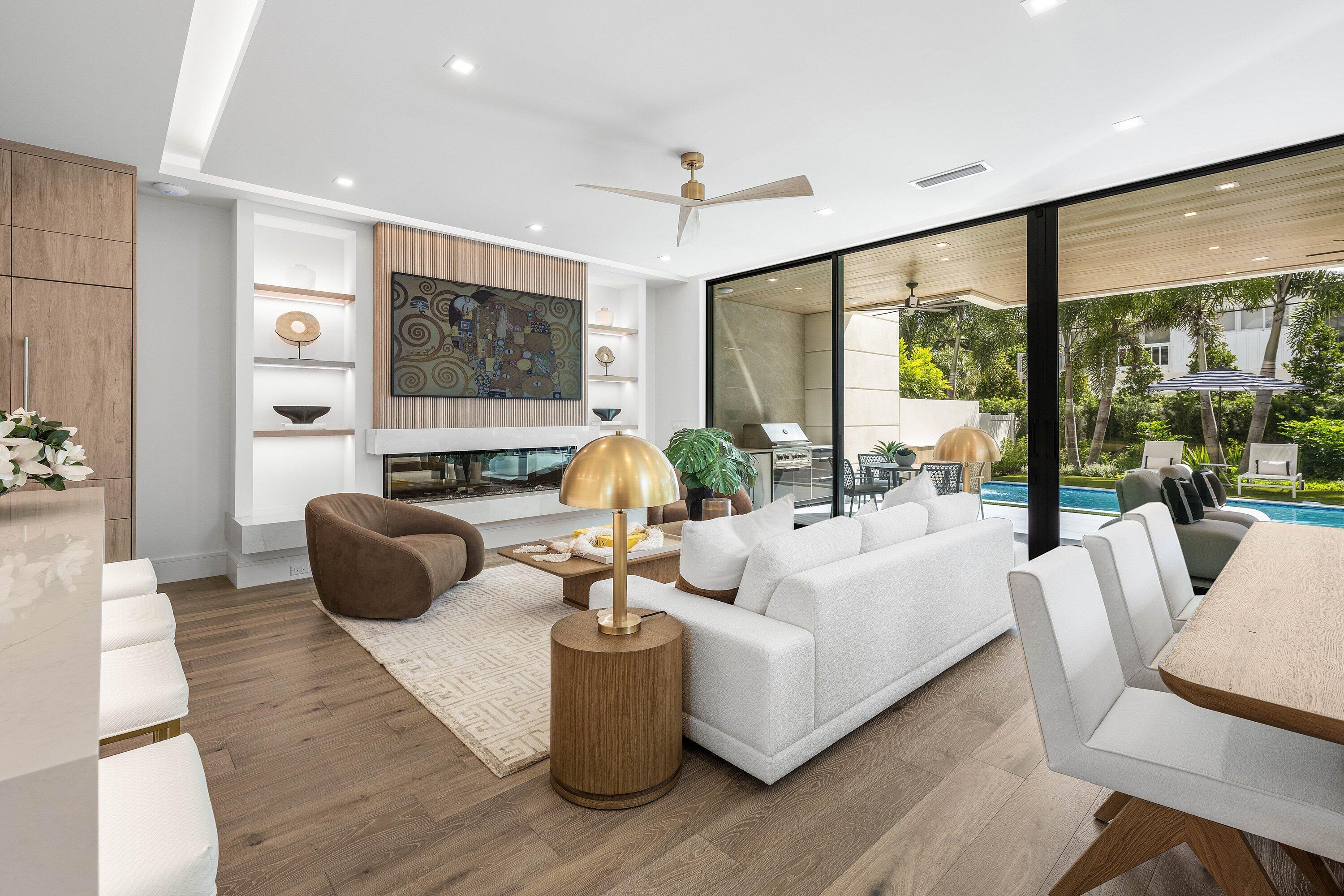 Contemporary living room with fireplace and white sectional opening onto a covered patio and pool.