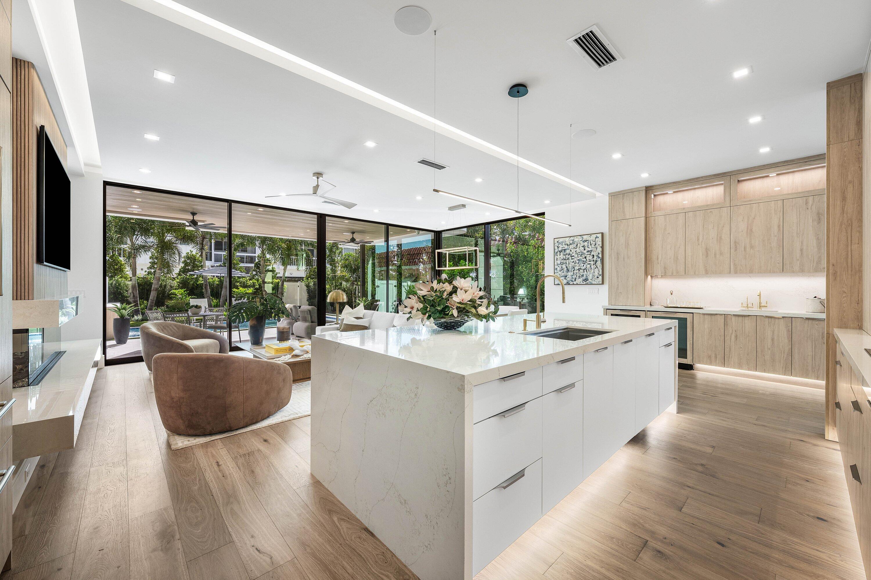 Open-plan kitchen with a large white island and glass doors overlooking a landscaped patio.
