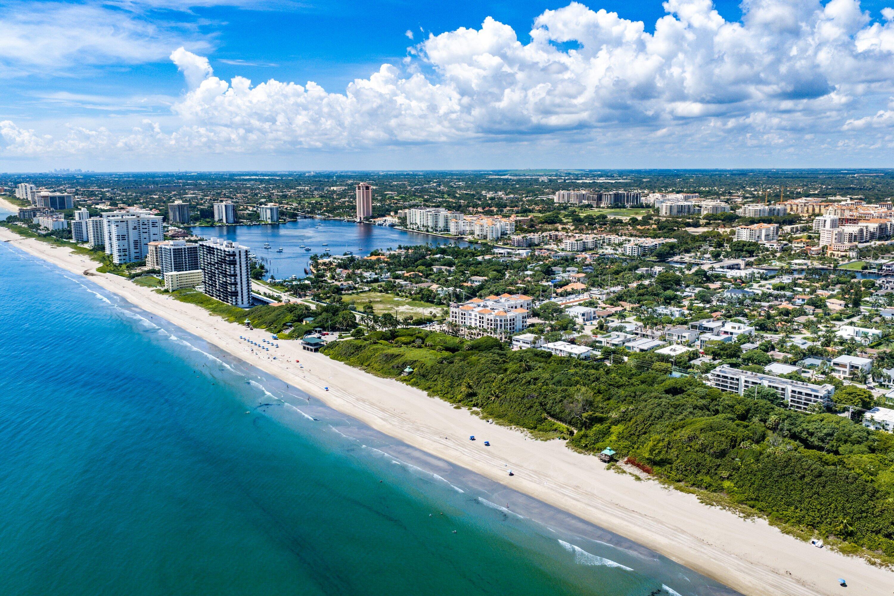 Aerial view of a sandy coastline, turquoise water, and coastal buildings.