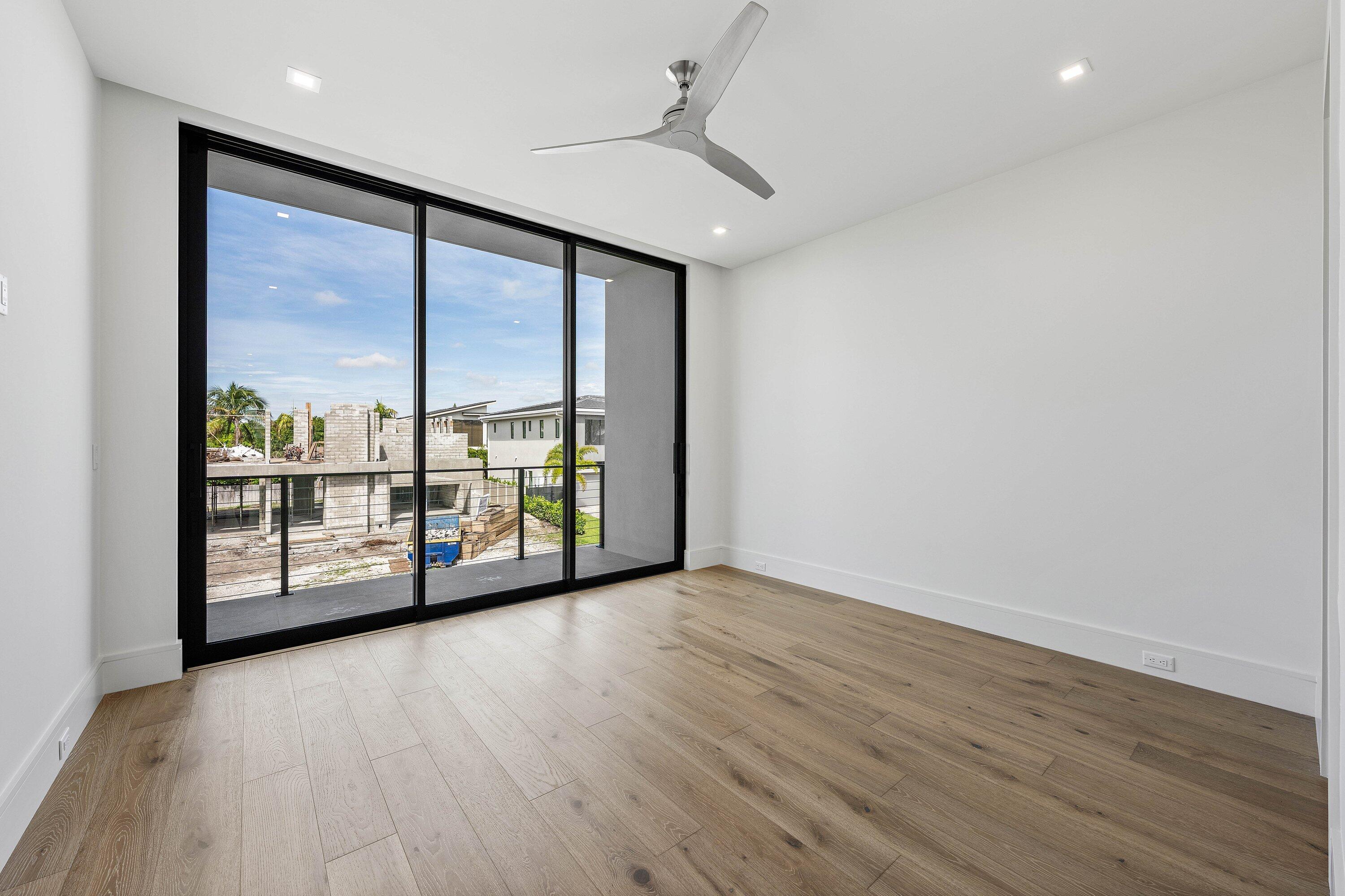 Empty room with wide-plank wood floors, a ceiling fan, and sliding glass doors to a balcony.