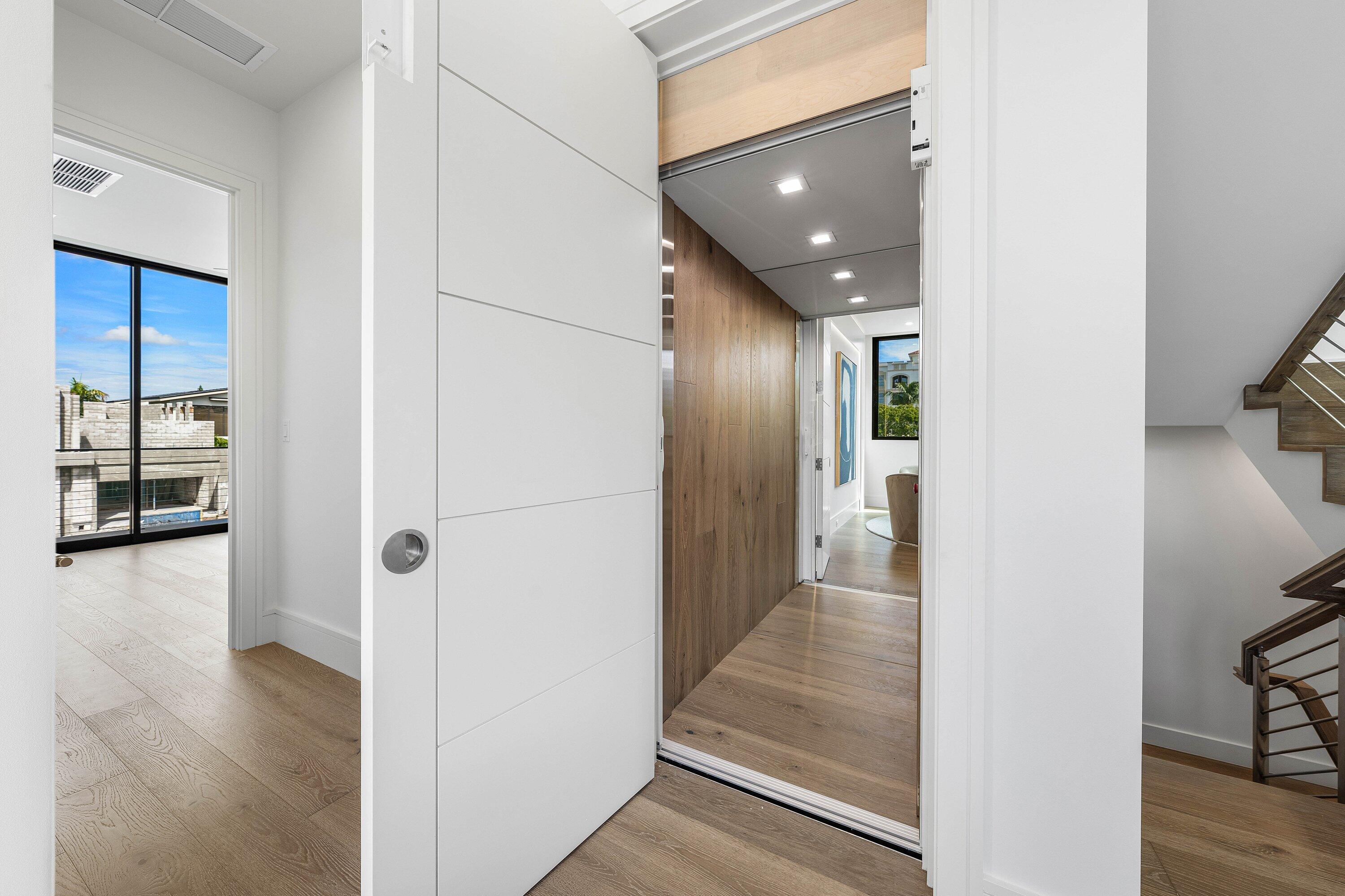 Modern entry hall with a large white sliding door, wood-paneled corridor, and open staircase.