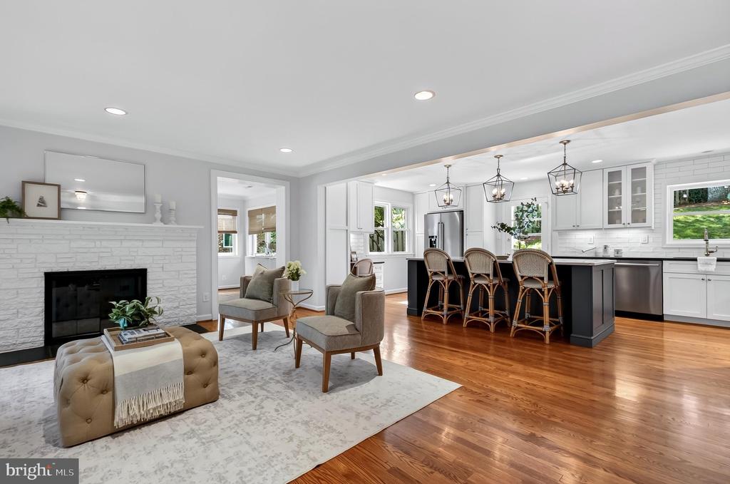 Open-plan living room and kitchen with a white stone fireplace, hardwood floors, and a dark island.