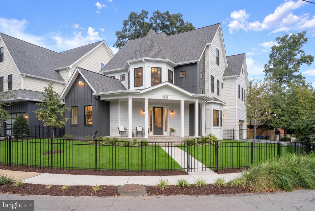 Two-story white and charcoal house with a covered porch, green lawn, and black metal fence.