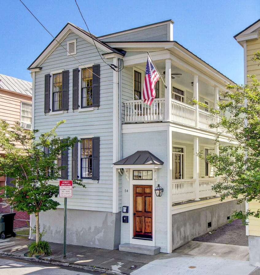 Light blue Charleston house with white wraparound porches, dark shutters, and an American flag.