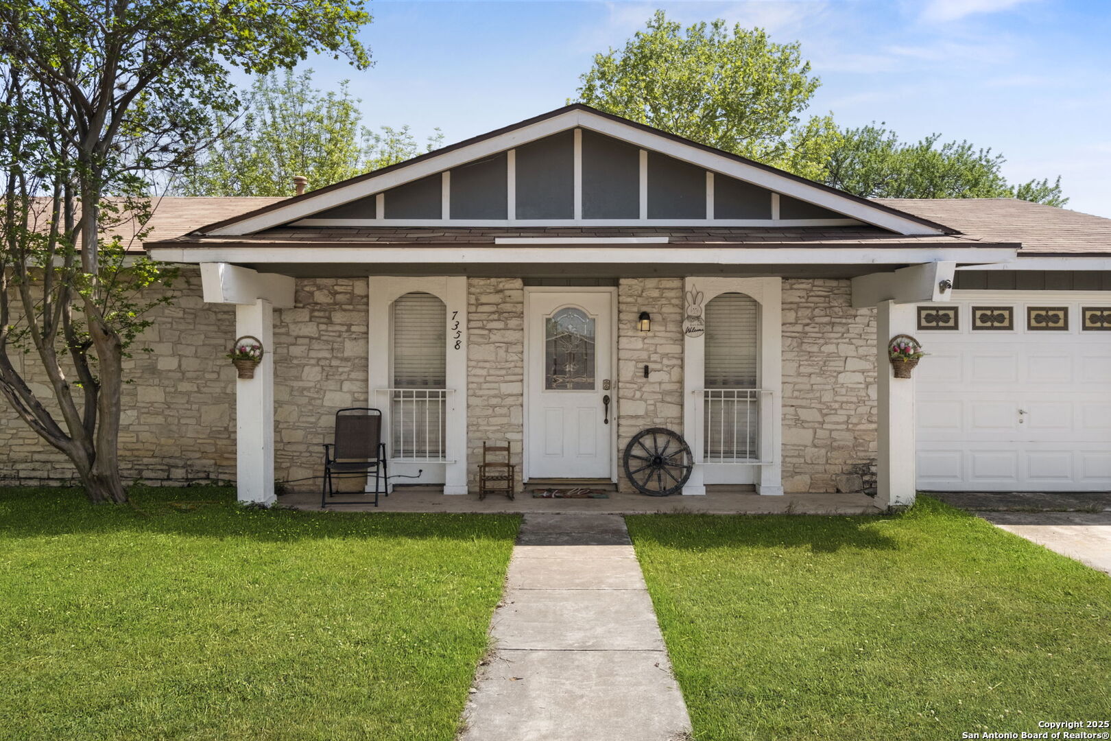 Stone-front home with a covered gabled porch, white entry door, and attached garage.