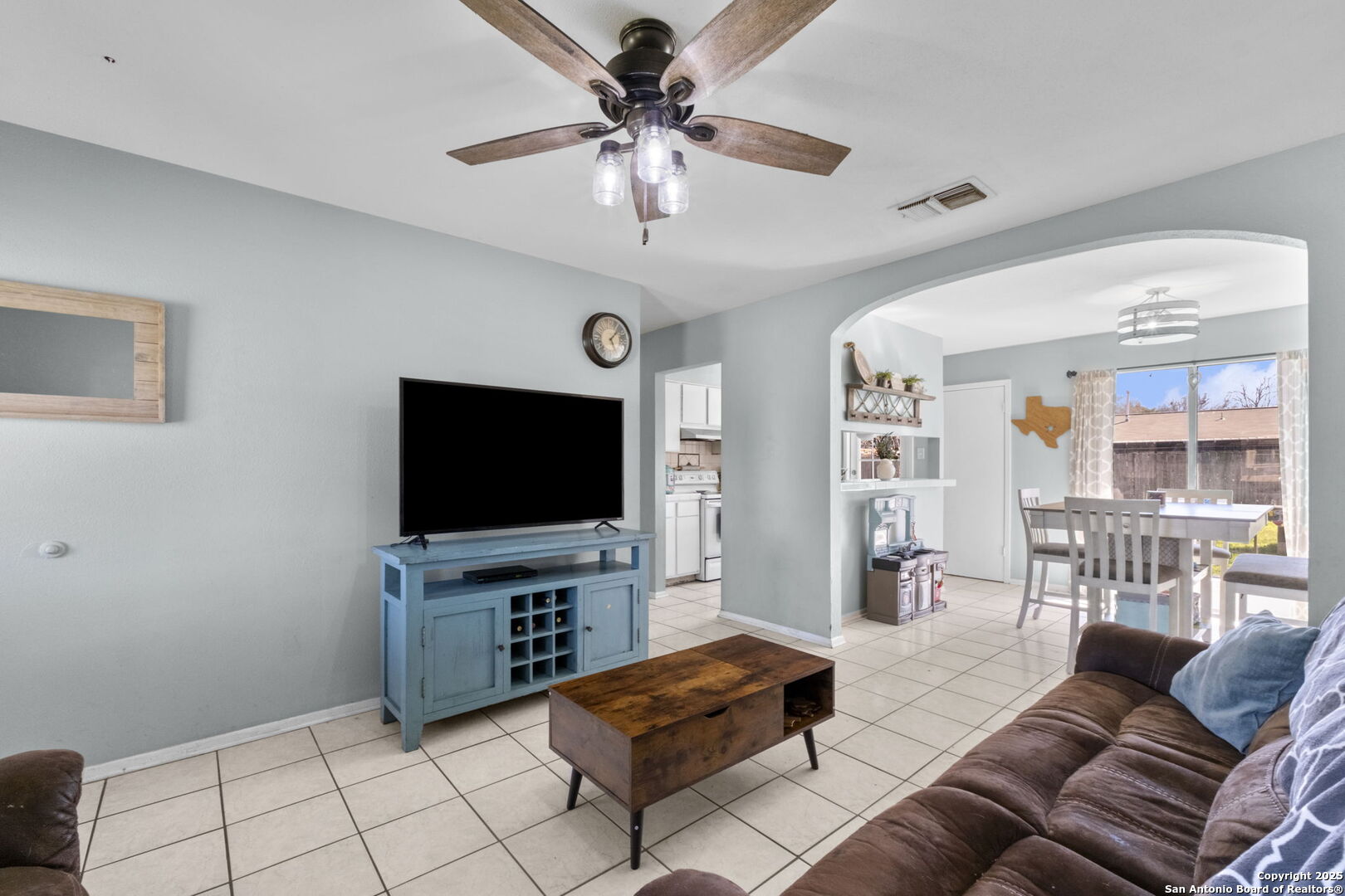 Living room with a blue TV console and an arched opening to a bright dining area.