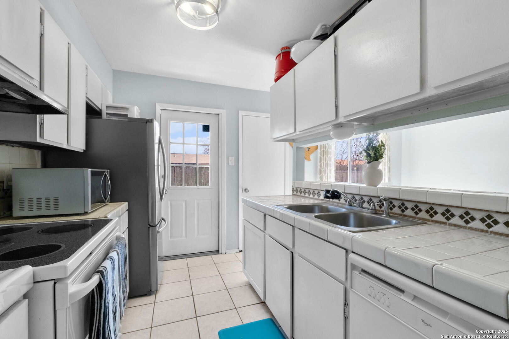 Kitchen with white cabinets, tiled counters, a double sink, and a glass-paneled back door.