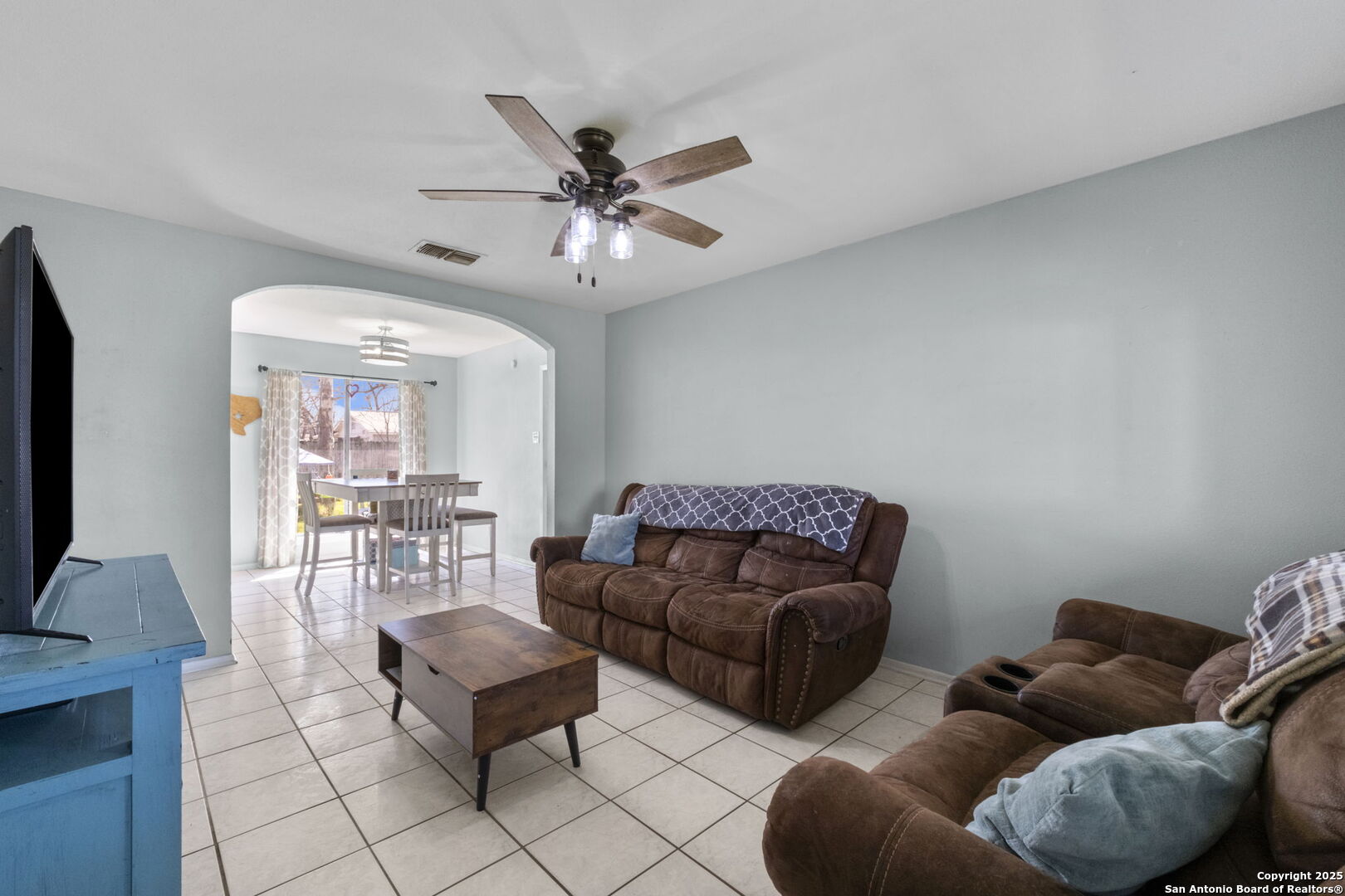 Living room with brown reclining sofas and an arched opening to the dining area.