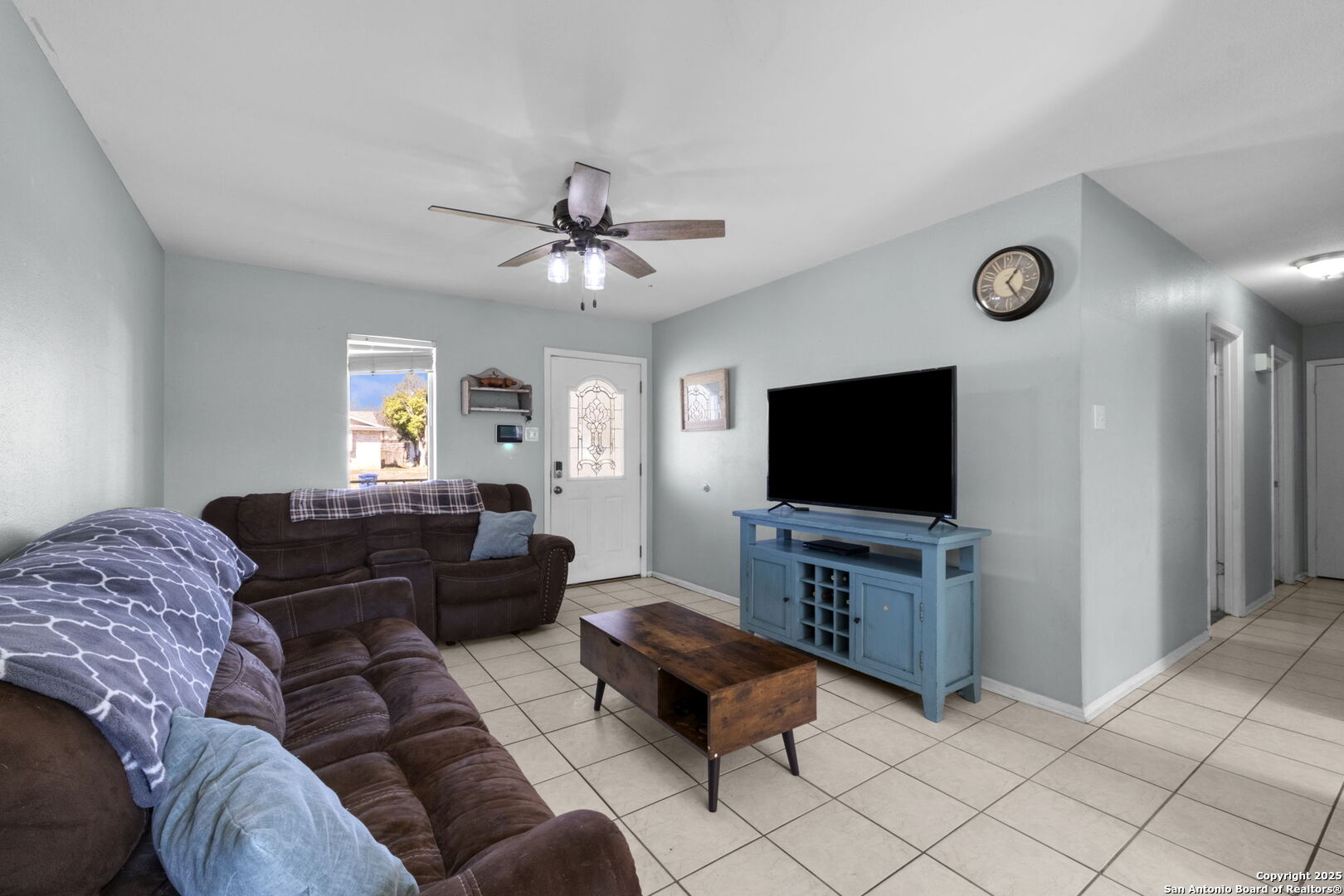 Living room with brown sofas, pale blue walls, tiled flooring, and a blue TV console.