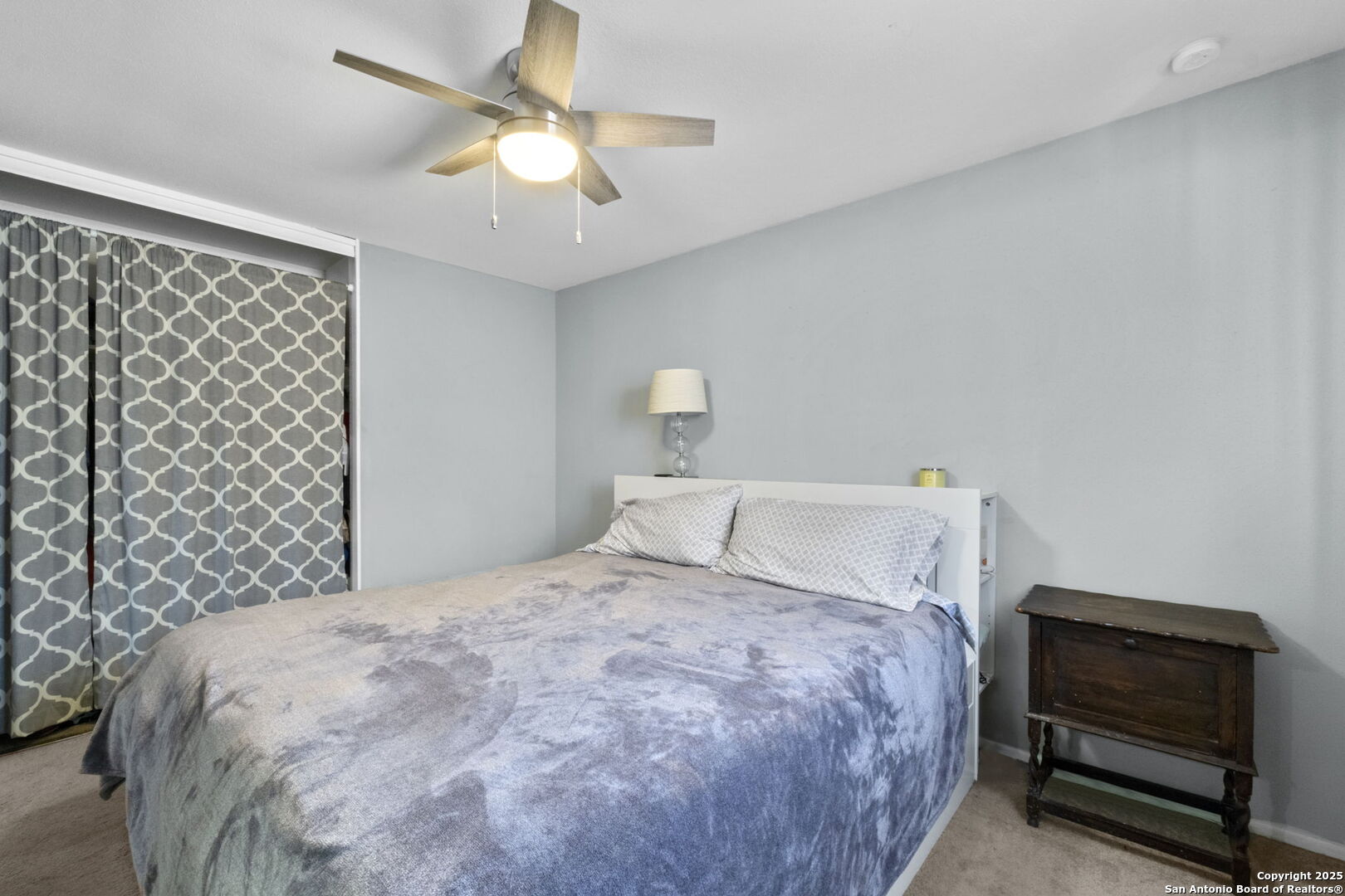Furnished bedroom with a large bed, patterned curtains, and a wooden bedside chest.