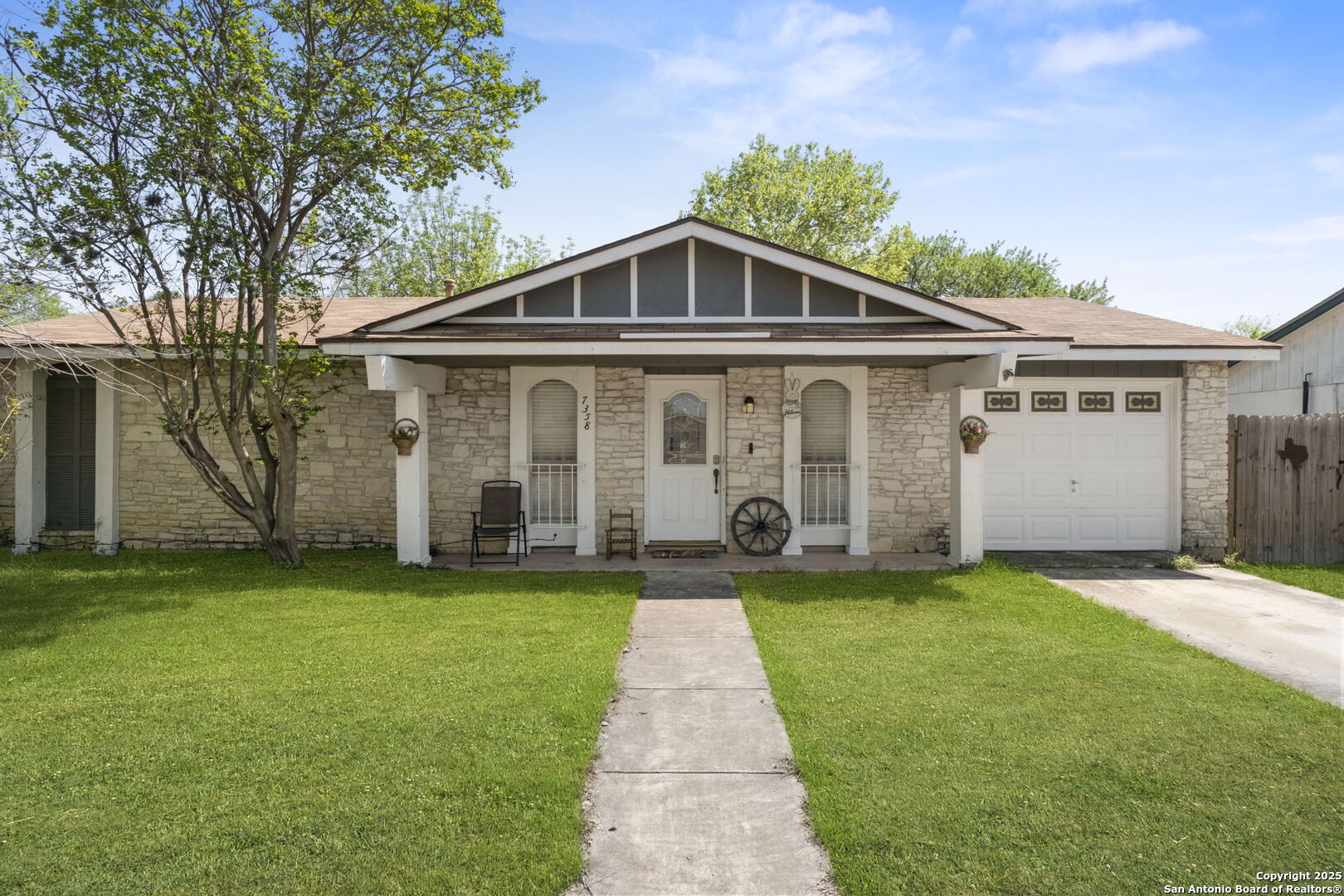 Stone-front single-story house with a gabled porch, attached garage, and walkway across the lawn.