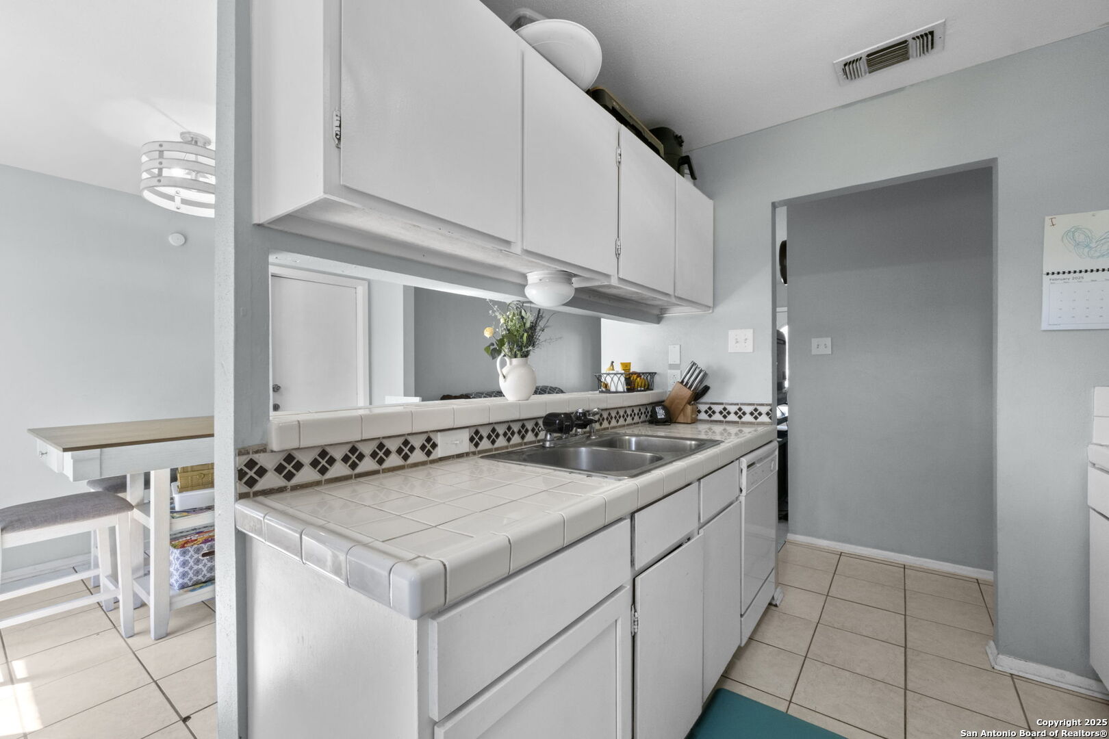 Kitchen with white cabinets, tiled counters and backsplash, and a double-basin sink.