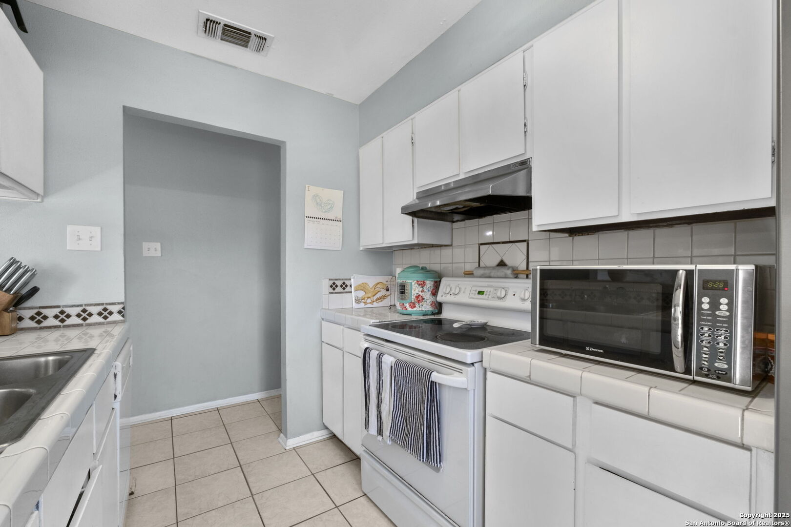 Kitchen with white cabinets, tiled counters, electric range, and countertop microwave.