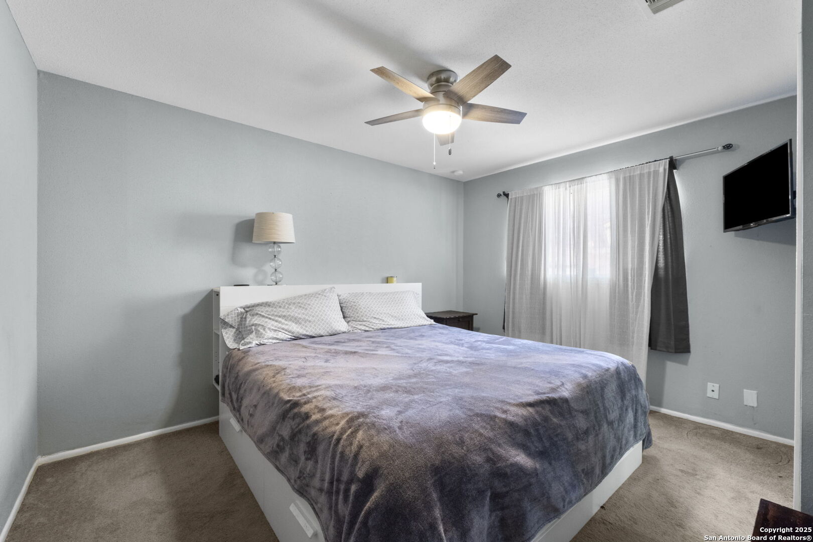 Furnished bedroom with a large bed, ceiling fan, and wall-mounted television.