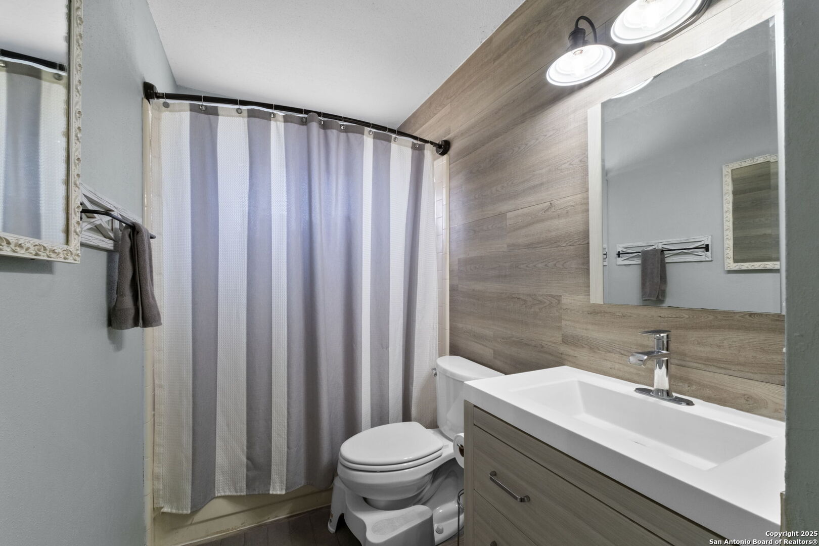 Bathroom with a wood-look accent wall, white vanity, and striped shower curtain.